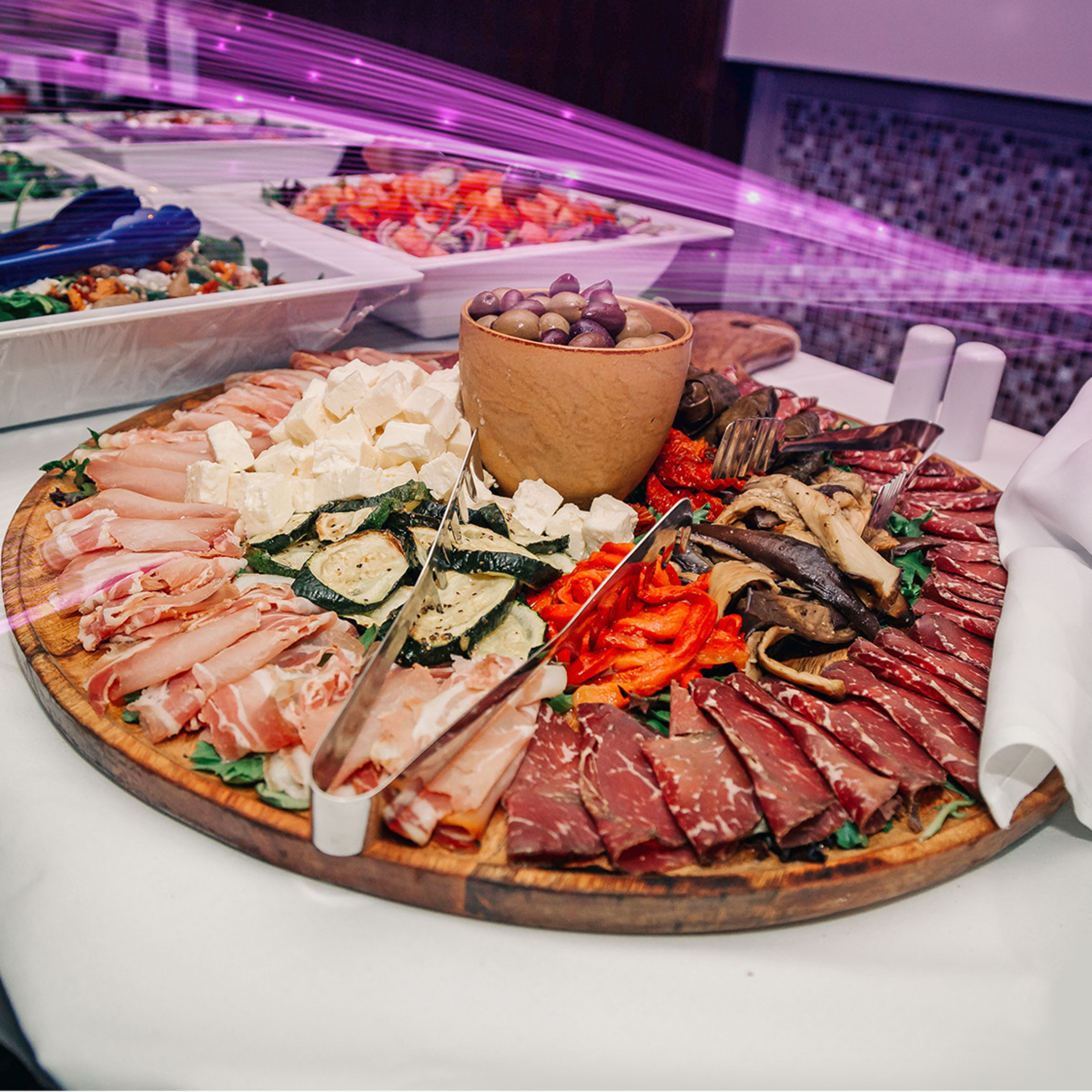 Large charcuterie board with meats, cheeses, olives, and vegetables arranged for a wedding reception buffet.