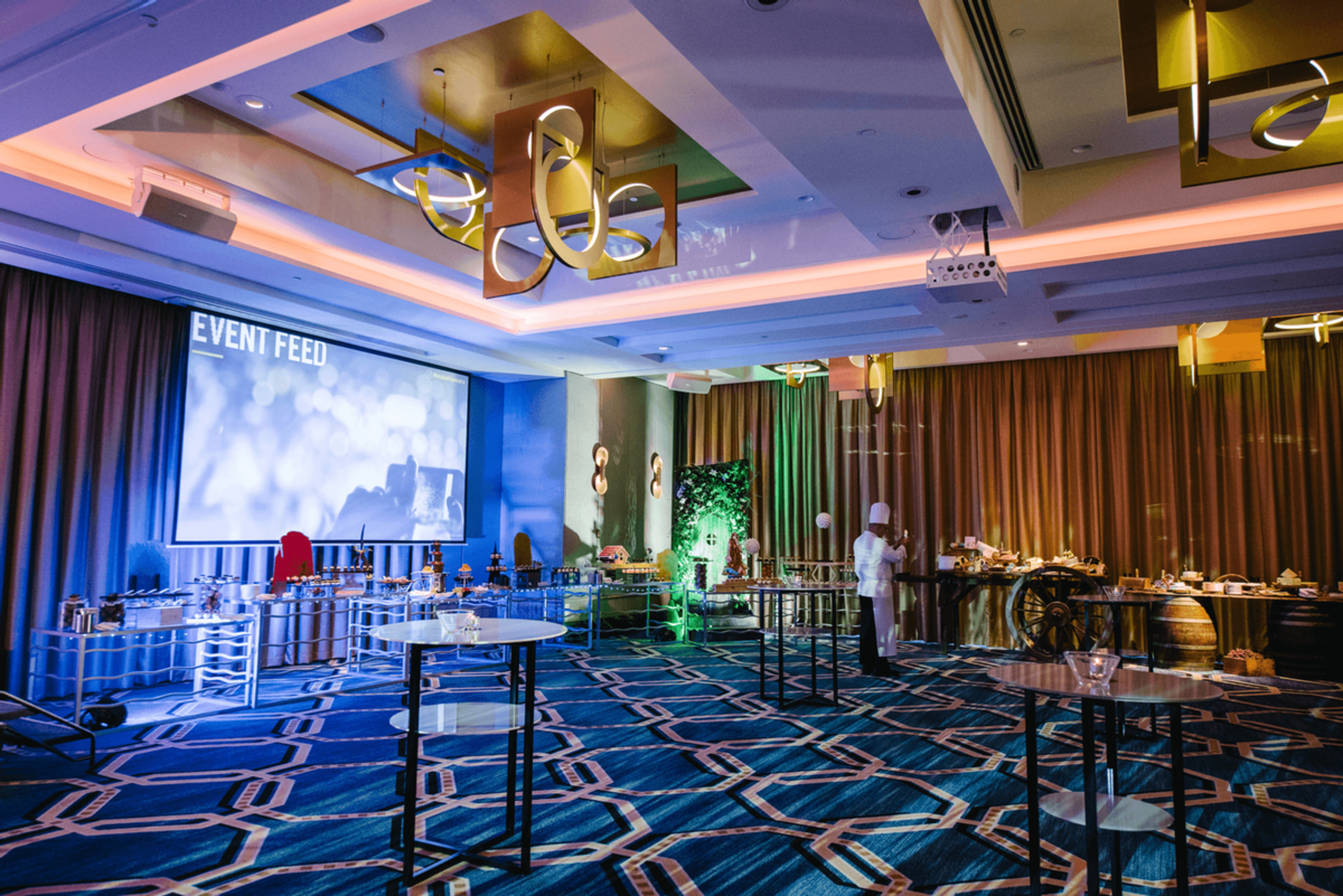Modern hotel ballroom set up for a wedding reception with buffet stations and colorful lighting.