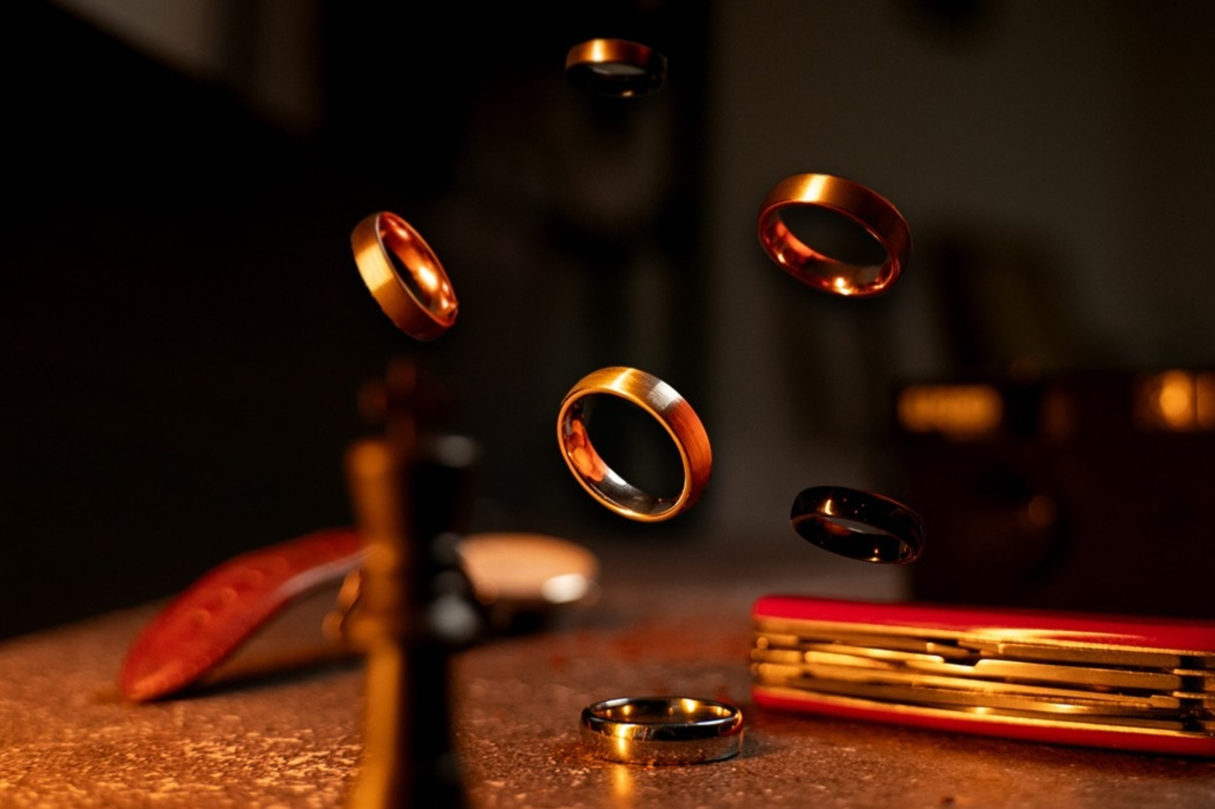 Floating gold and black wedding bands captured in dramatic warm lighting on a rustic surface.