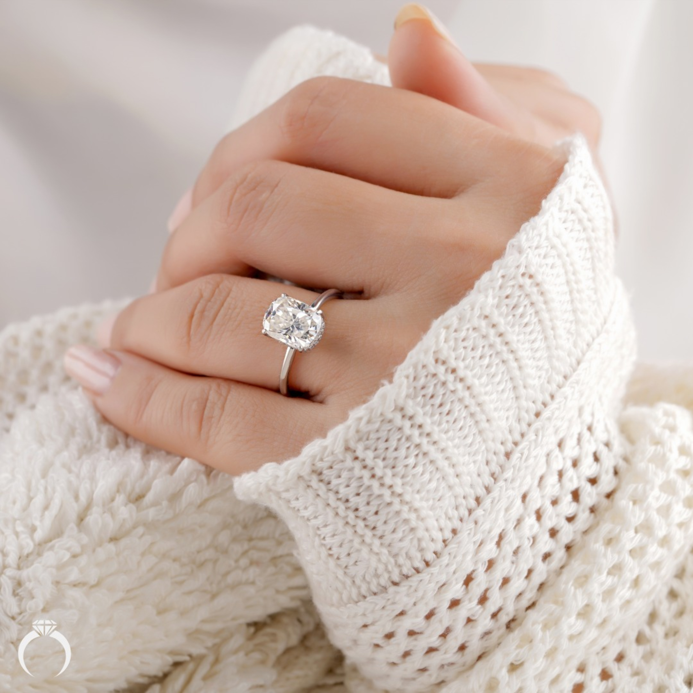 Close-up of a hand in a cozy knit sweater wearing a solitaire oval diamond engagement ring.