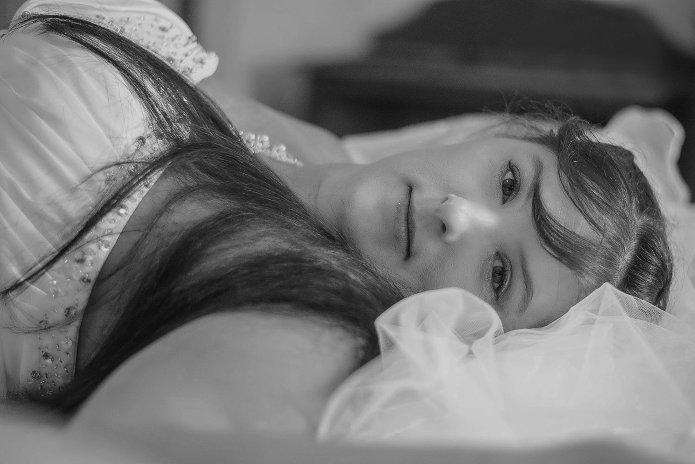 Black and white close-up portrait of a bride lying down with her veil and beaded gown.