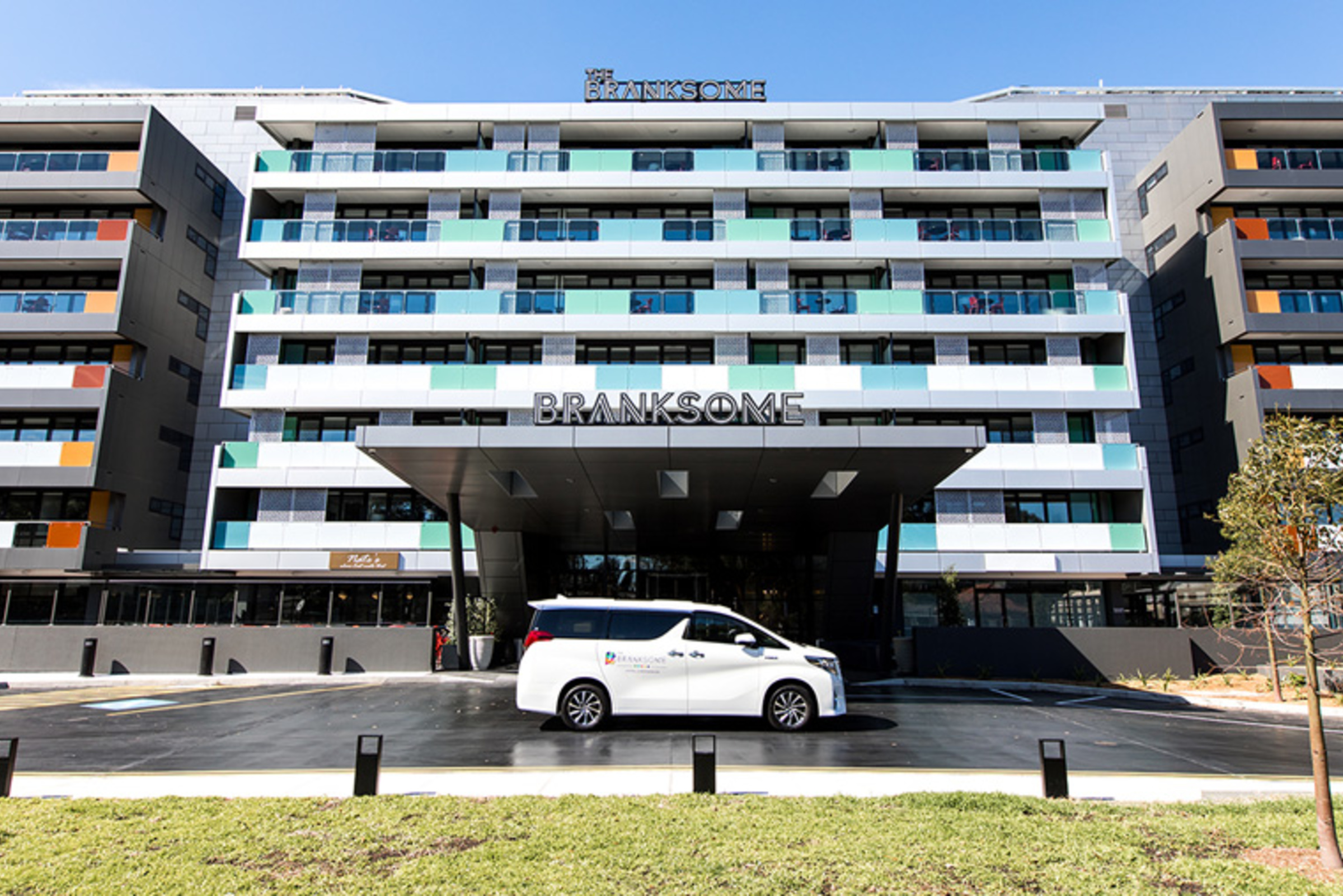 Modern hotel entrance with a branded white shuttle van parked in front of The Branksome building.