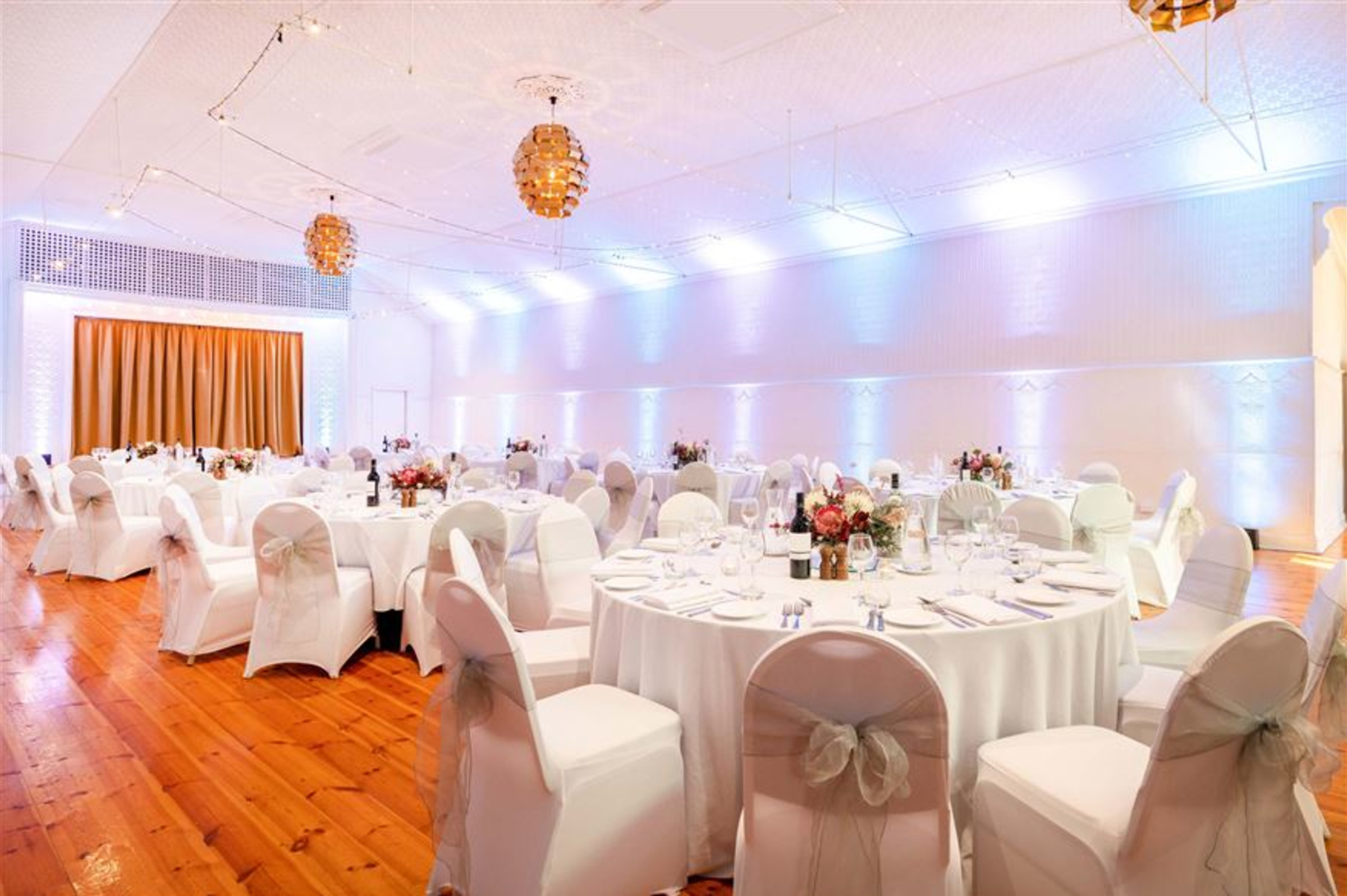 Elegant indoor wedding reception setup with round tables, white chairs, and warm ambient lighting.
