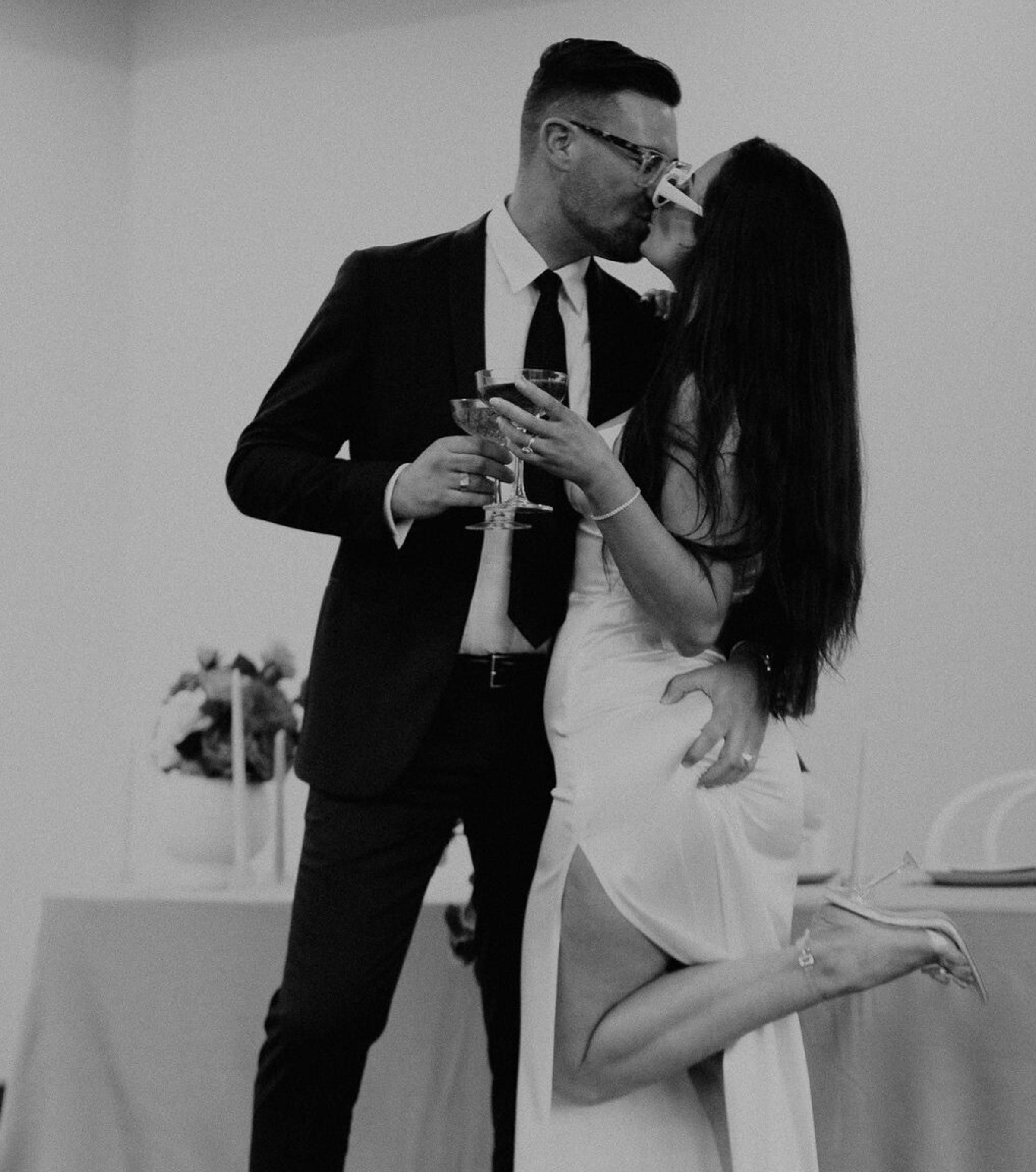 Black and white photo of a couple kissing and toasting with champagne at their wedding reception.