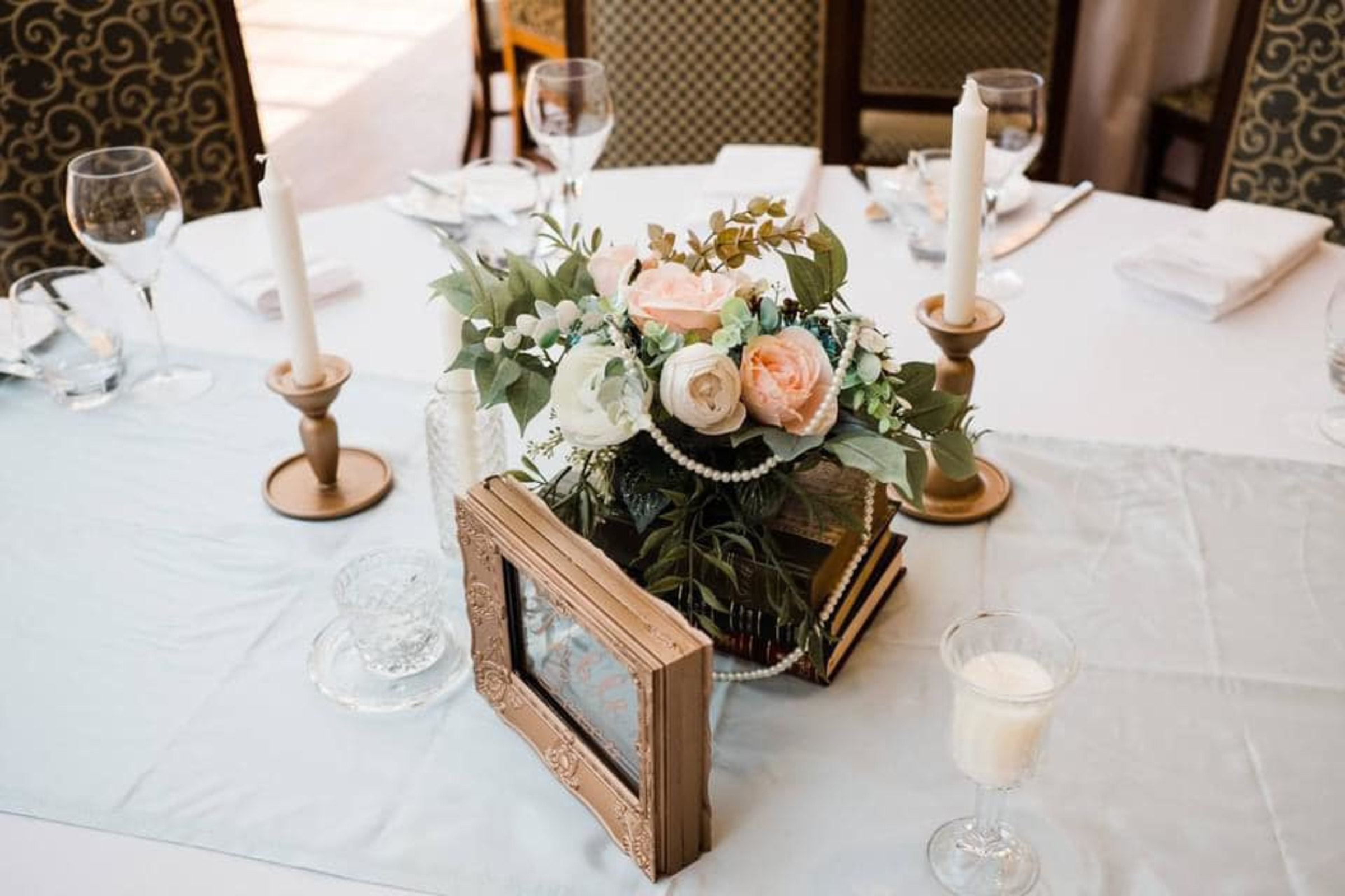 Romantic wedding reception table with floral centerpiece, vintage books, candles, and pearls.