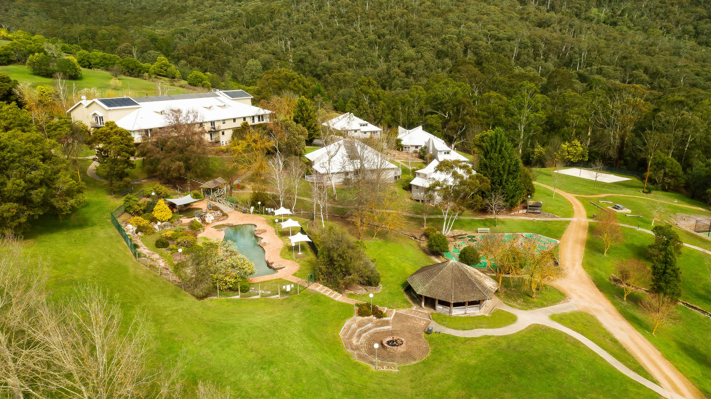 Aerial view of a countryside wedding venue with lodges, gardens, pool and forest surroundings.