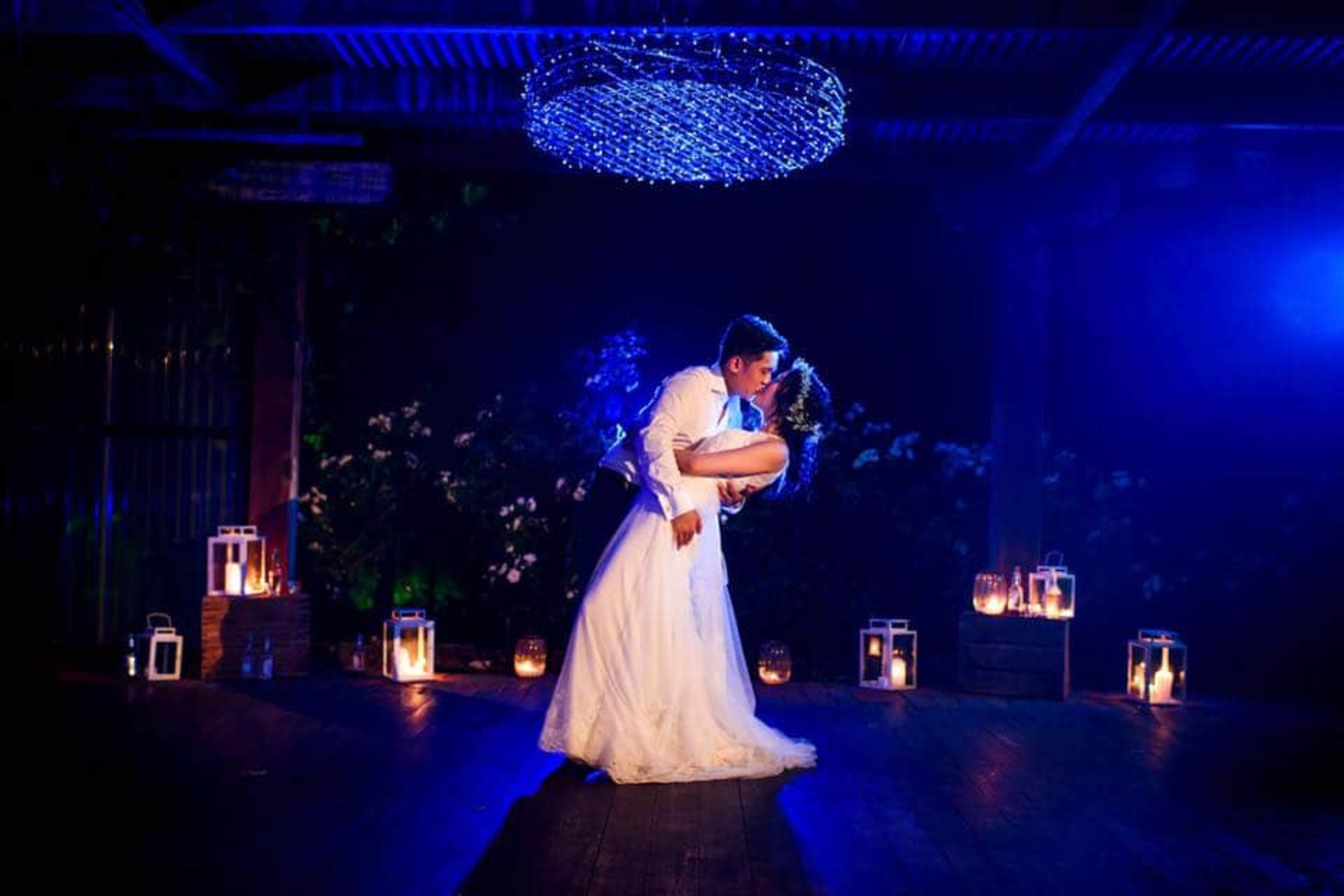 Bride and groom share a romantic night-time dance surrounded by lanterns and blue lighting.