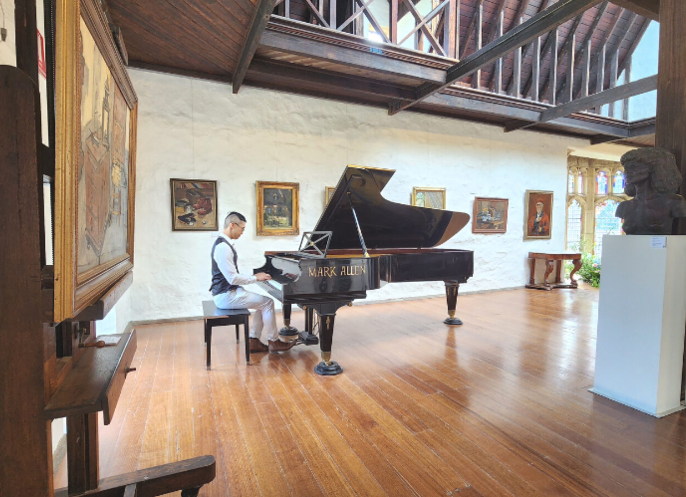 Pianist playing a grand piano in an elegant art gallery with wooden floors and paintings on the walls.