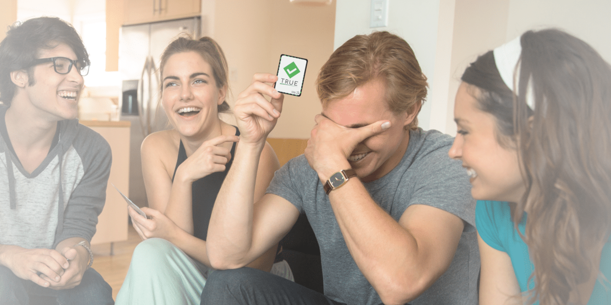 Group of friends laughing and playing a card game together indoors