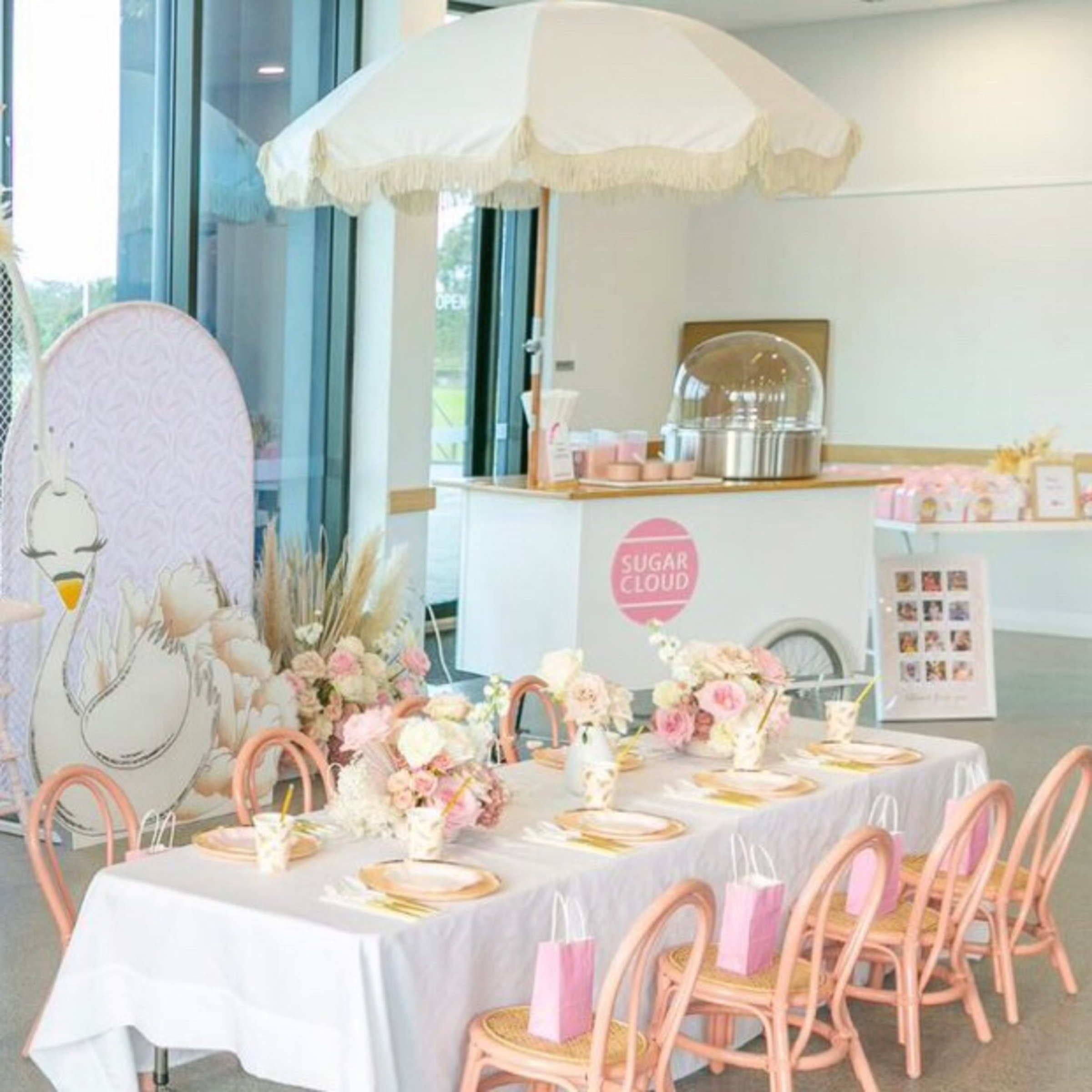 Pastel pink and white wedding dessert setup with a cotton candy cart and elegantly decorated table.