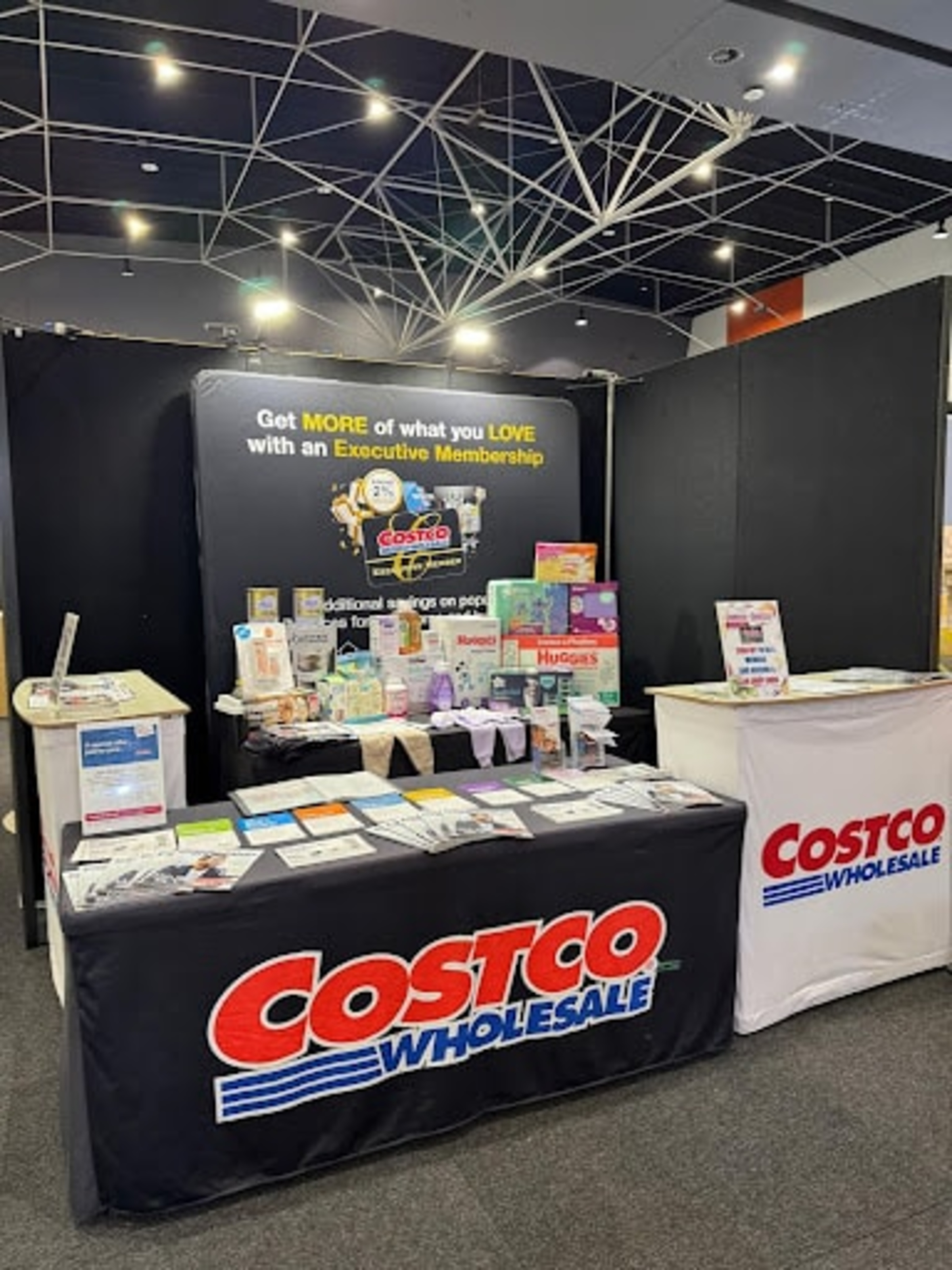 Costco Wholesale booth at a wedding expo displaying membership offers and product samples on tables.