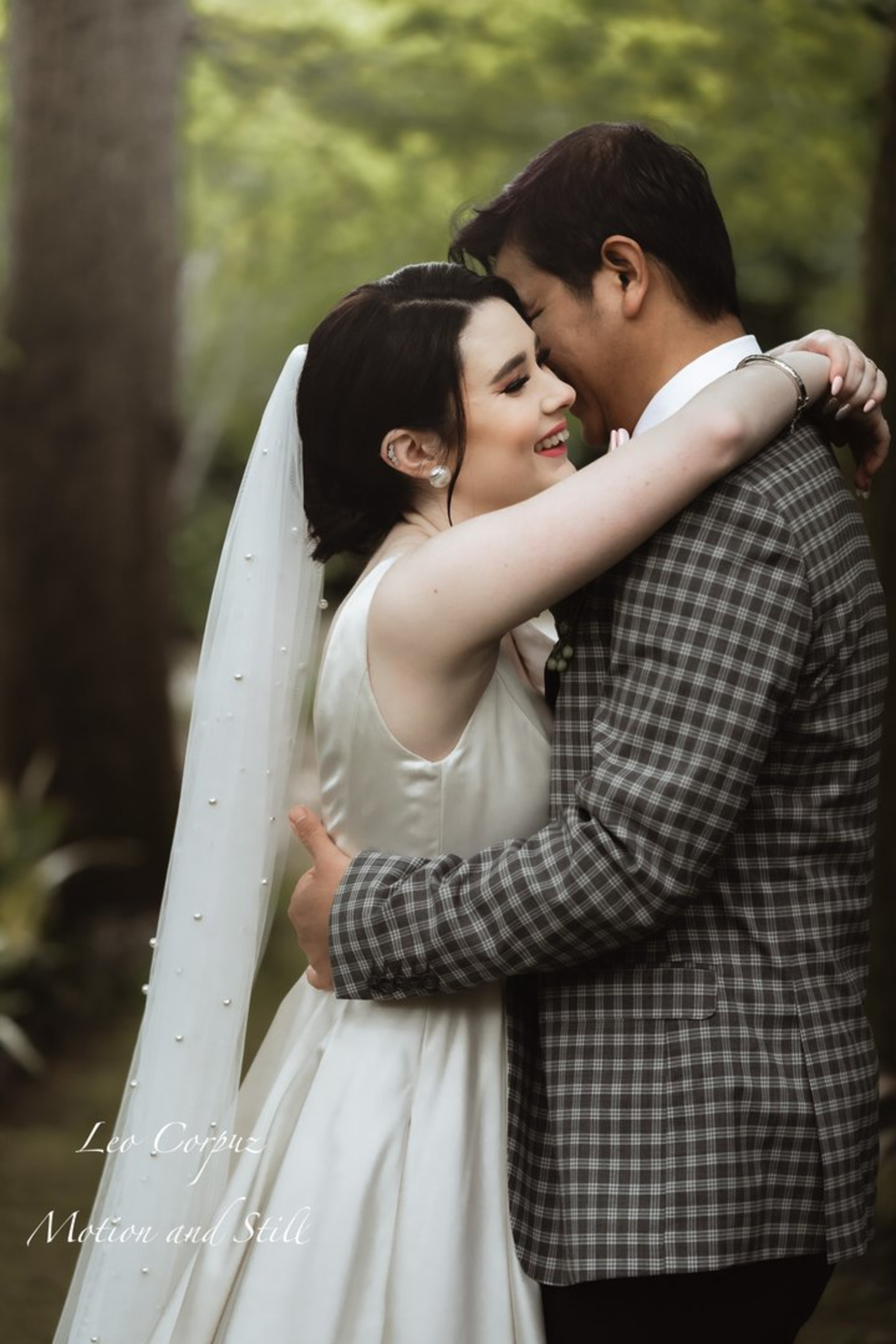Bride and groom embrace and smile during an intimate outdoor wedding portrait in a lush green setting.