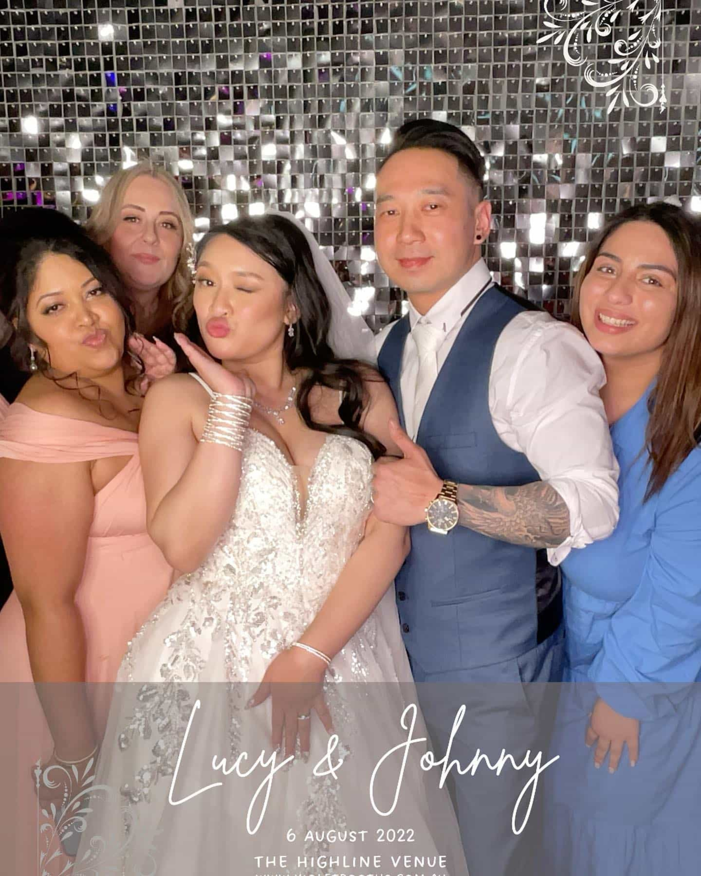 Bride, groom, and friends pose playfully in front of a sparkling silver backdrop at the wedding reception.