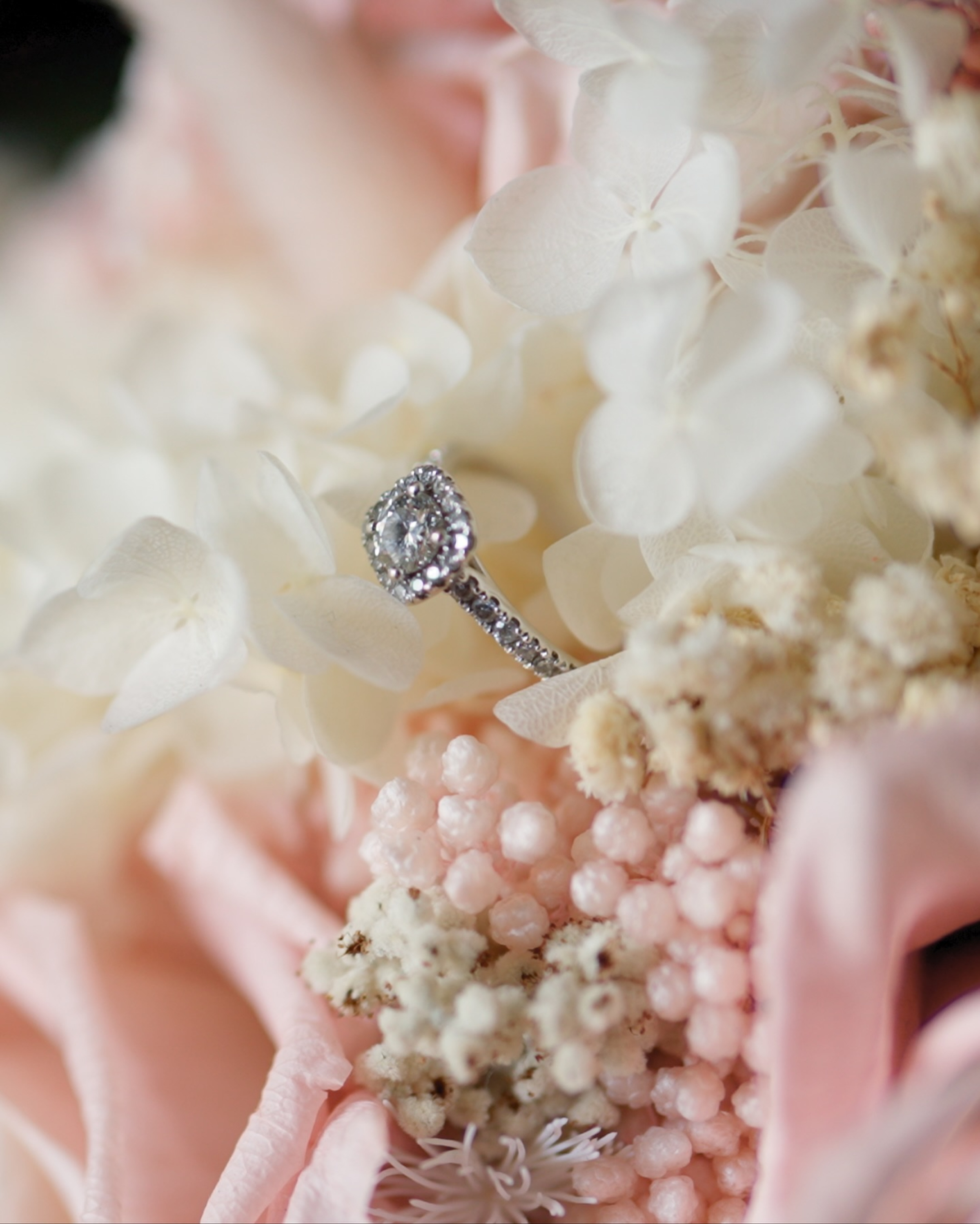 Diamond engagement ring nestled among soft pink and ivory wedding flowers.