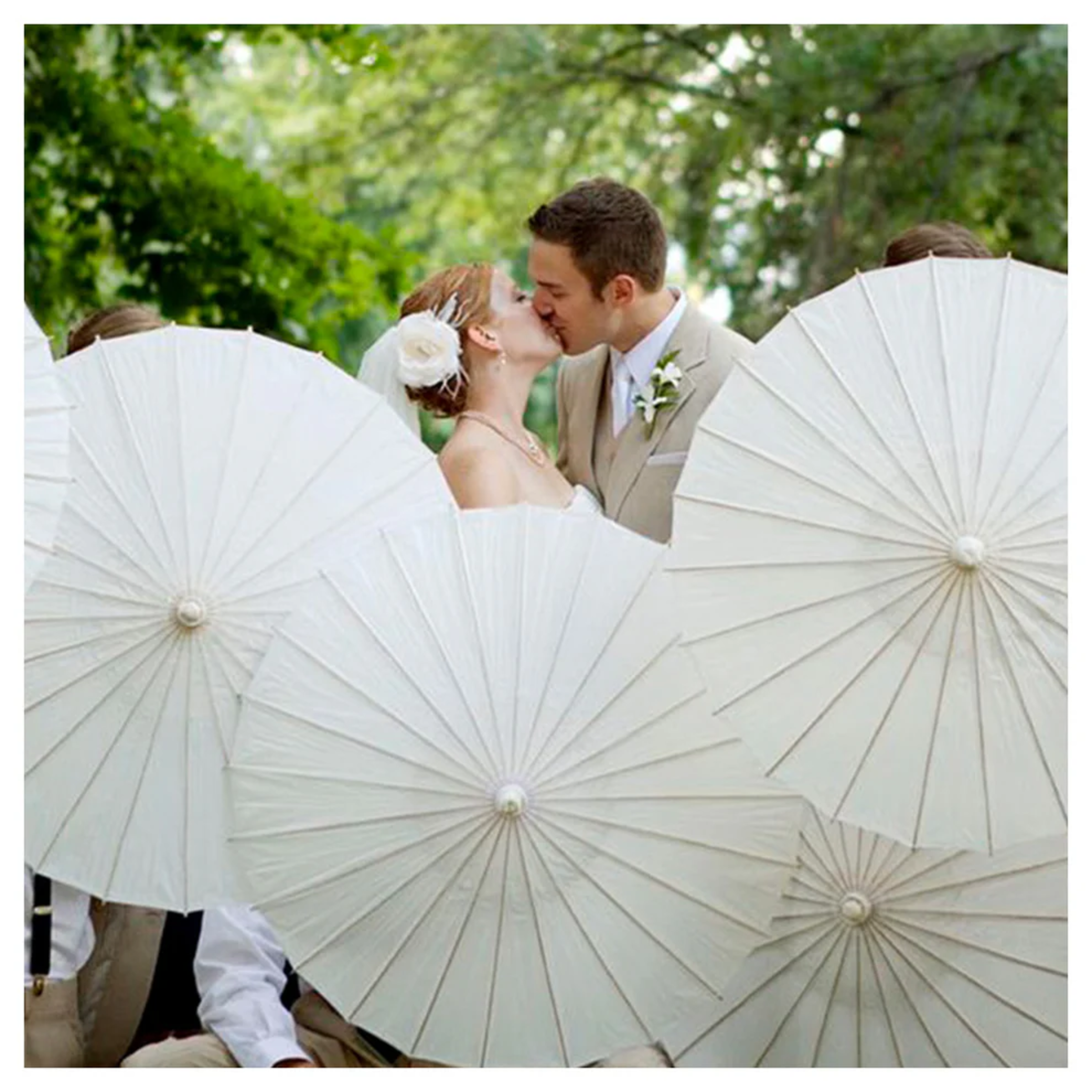 Bride and groom share a kiss behind white parasols at an outdoor wedding.