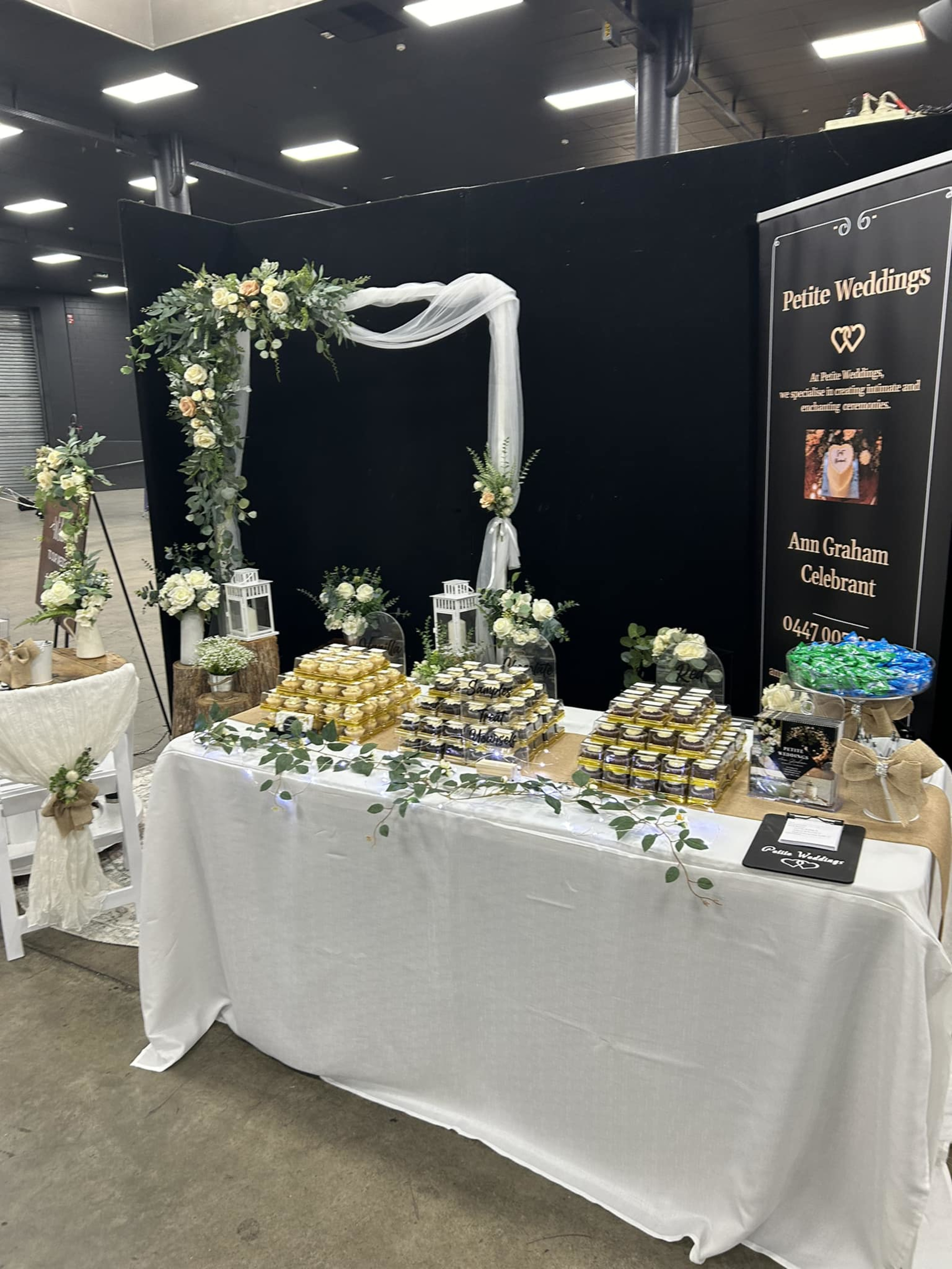 Rustic wedding expo display with floral arch, lanterns, and a table of favors for Petite Weddings.