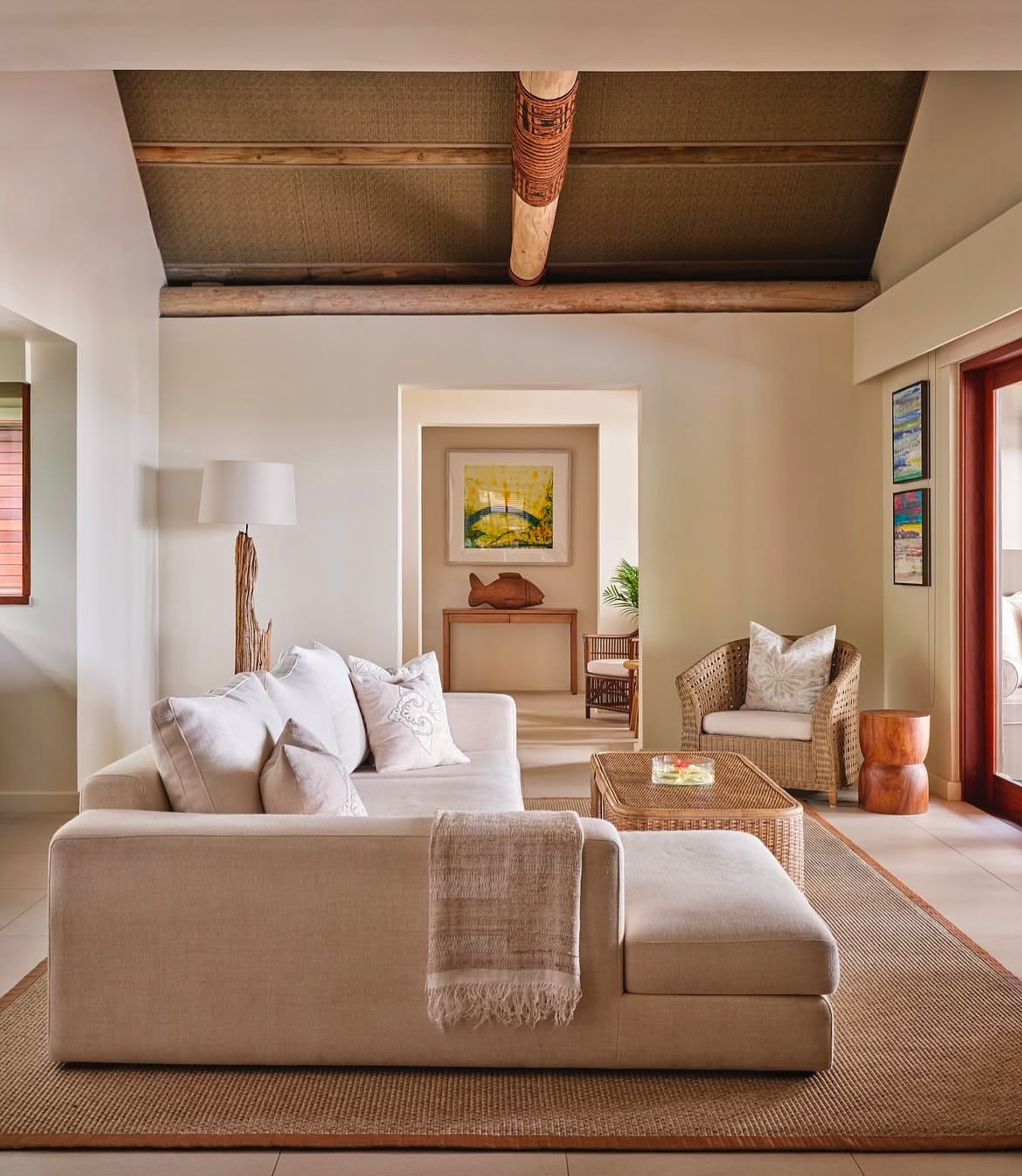 Neutral-toned resort-style living room with cream sofa, woven accents, and high wood-beam ceiling.