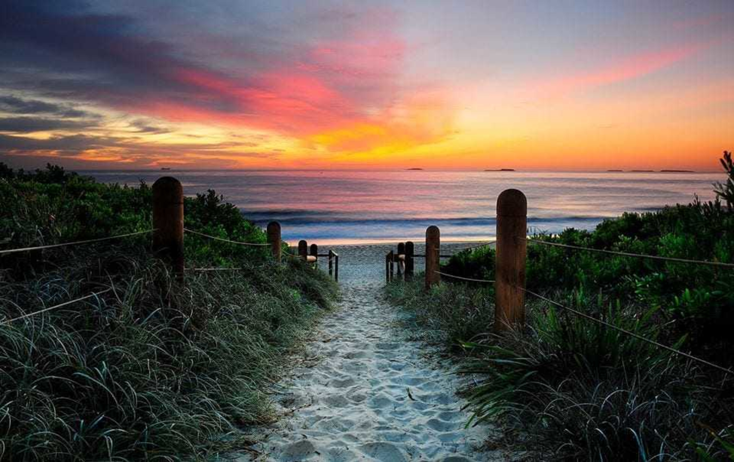 Sandy path leading to a tranquil beach at vibrant sunset over the ocean.