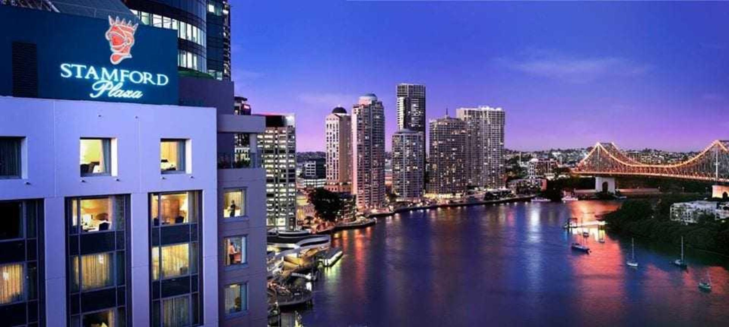 Riverside hotel overlooking a lit city skyline and bridge at dusk, ideal as an urban wedding venue.