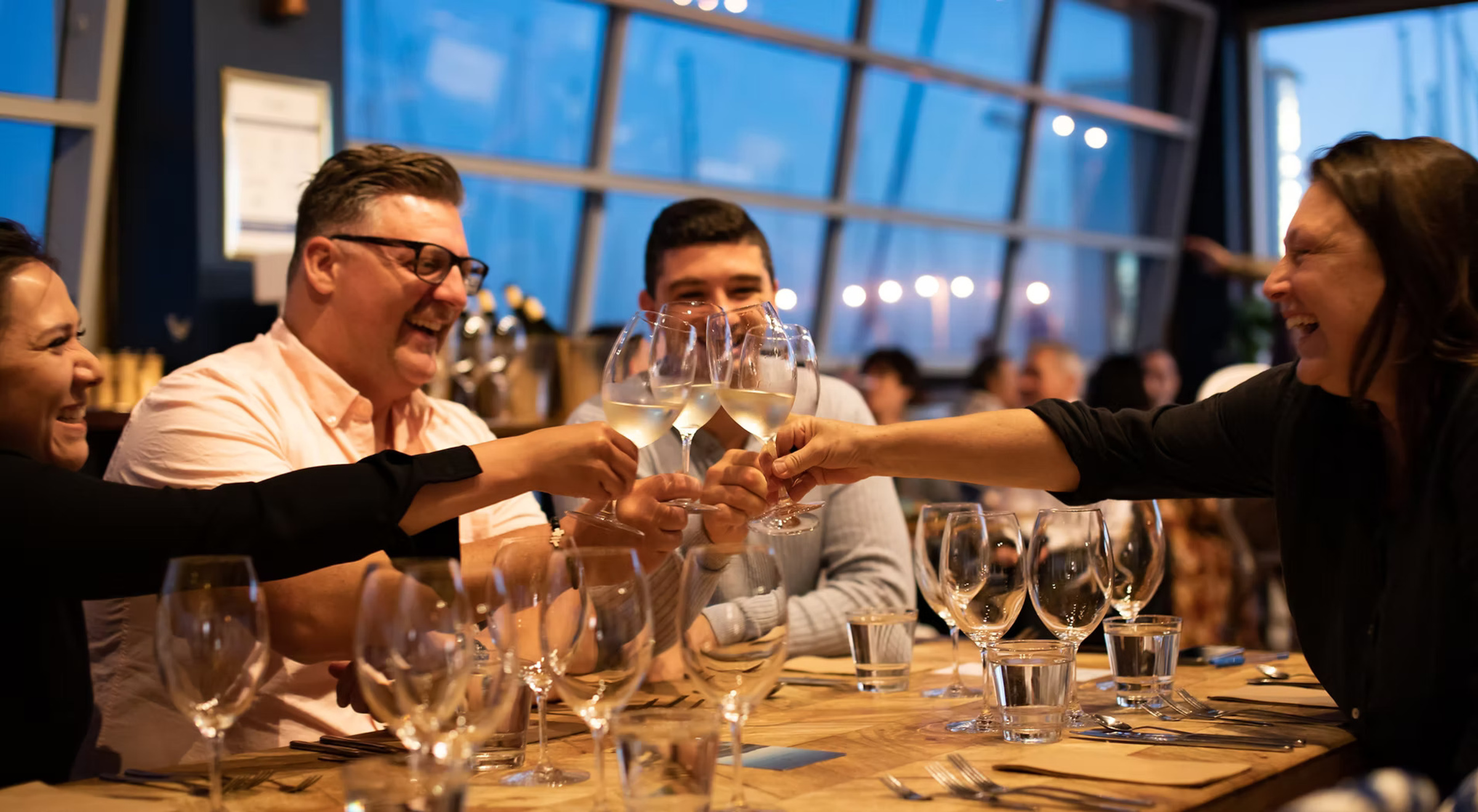 Guests raise wine glasses in a cheerful toast at a warmly lit wedding reception table.