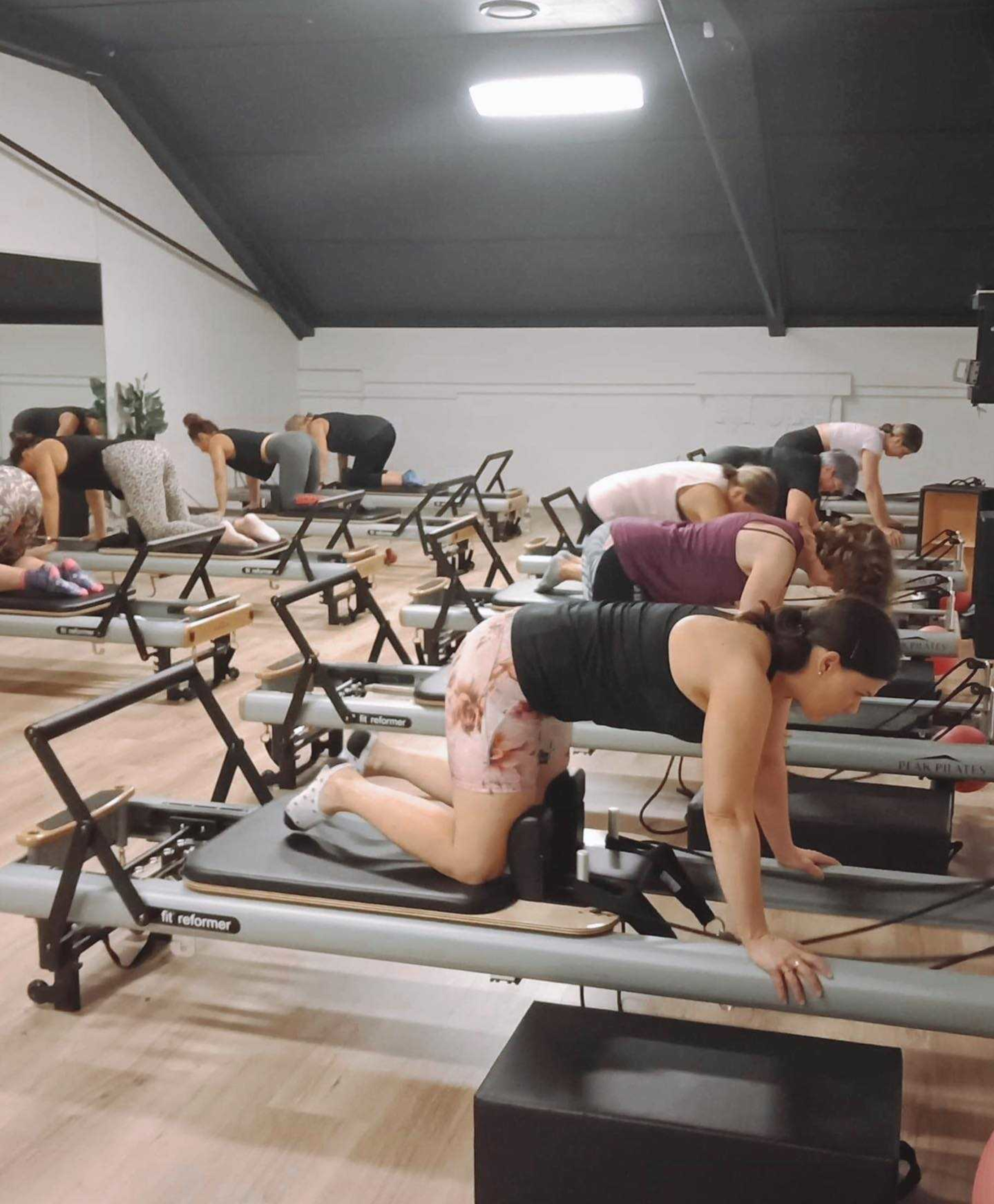 Group of people in a studio doing exercises on Pilates reformer machines.