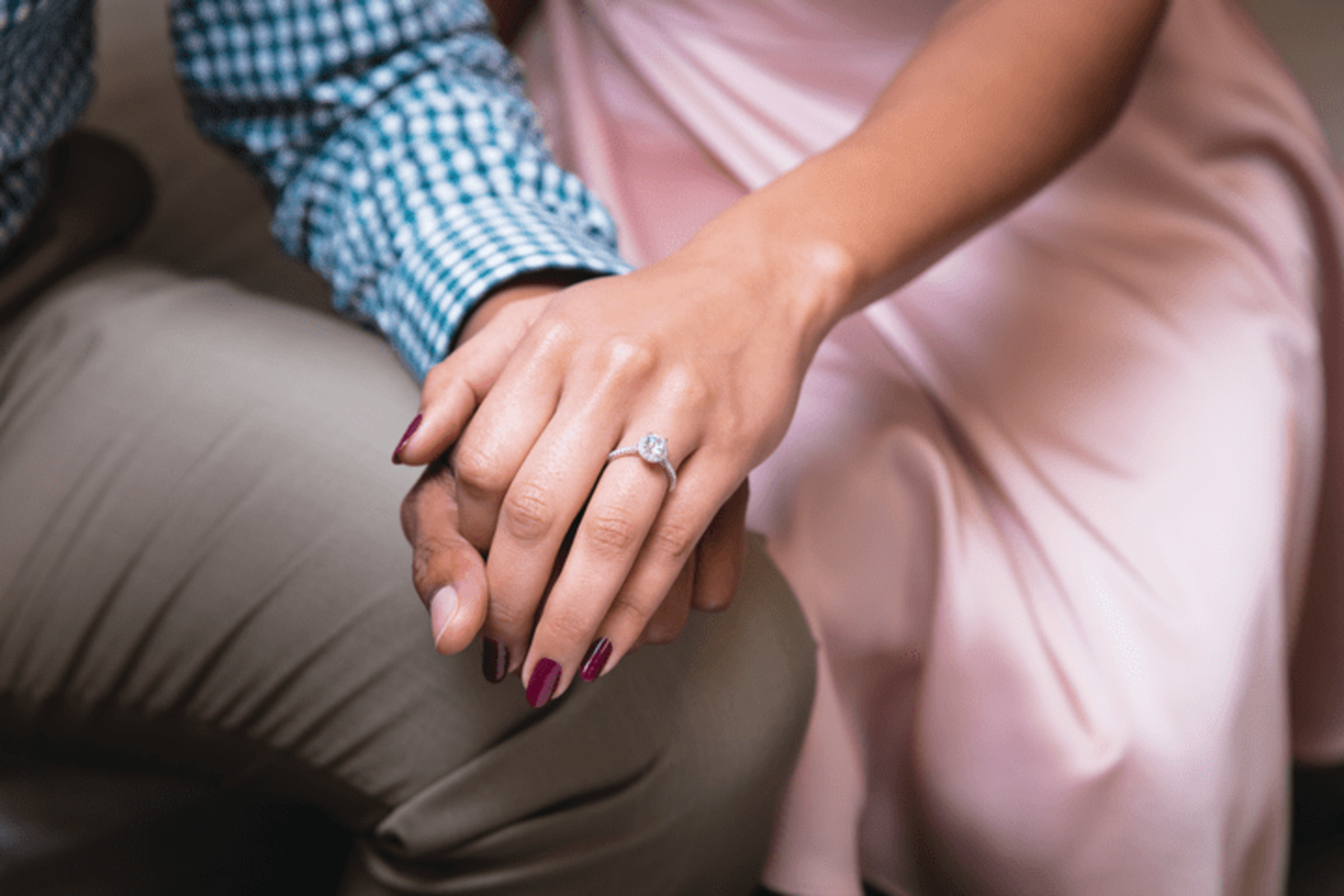 Close-up of a couple holding hands, highlighting a diamond engagement ring on her finger.