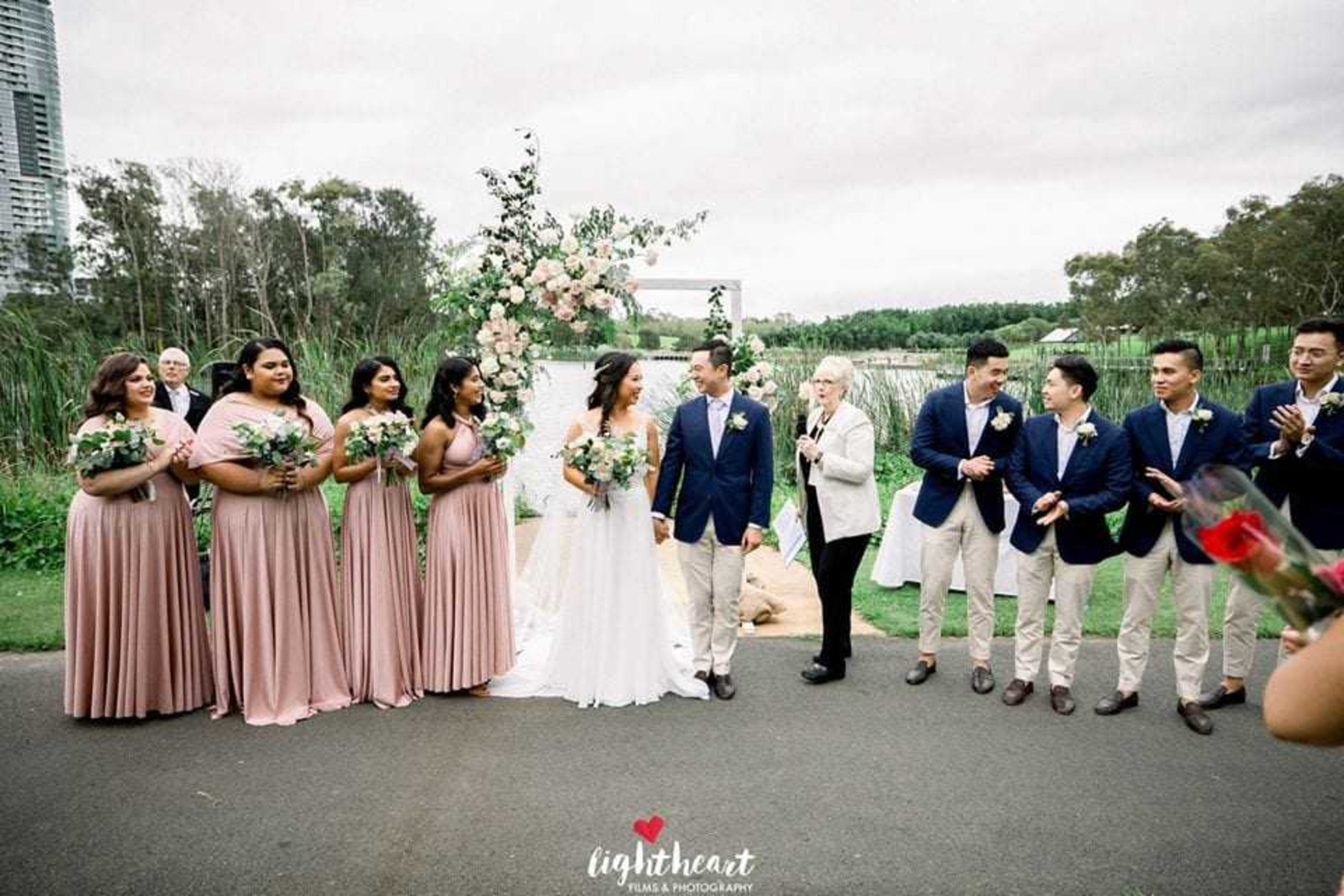 Outdoor waterfront wedding ceremony with a couple and their wedding party standing by a floral arch.