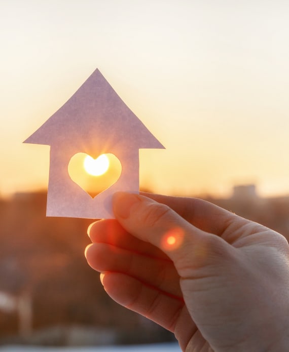 someone holding a cutout of a house against the sun