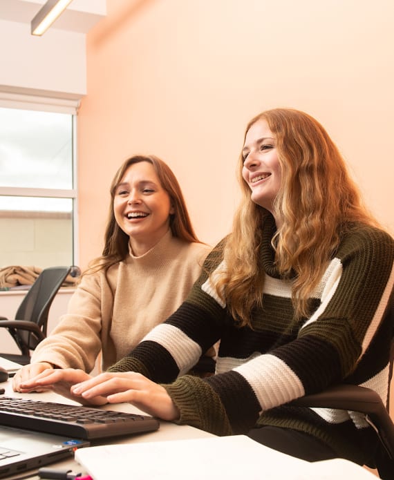 two smiling young girls sitting in front of laptop