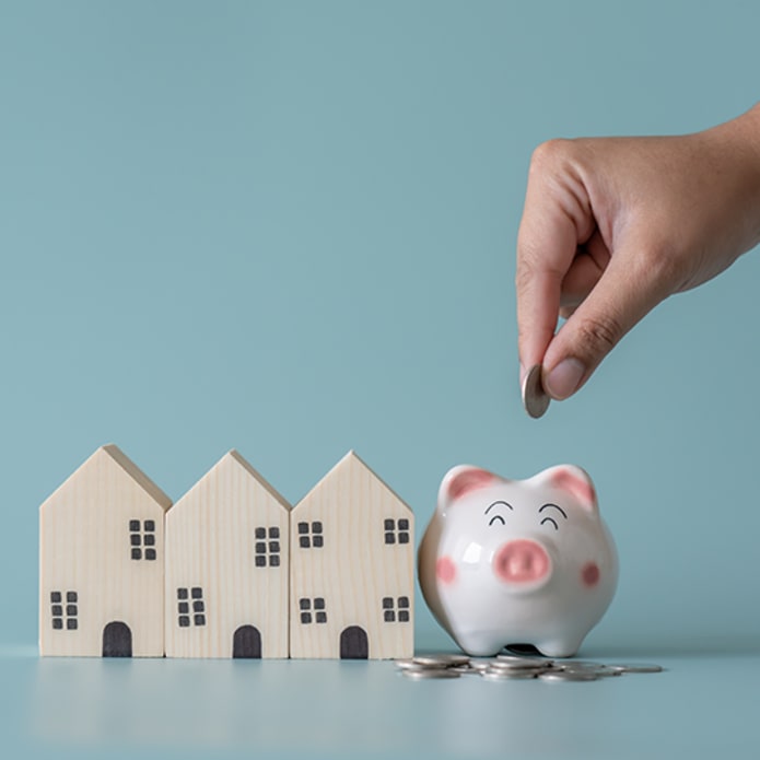 Small wooden houses next to a piggy bank being filled with coins