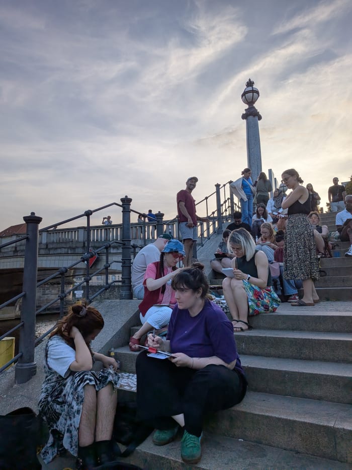 Sketchers sitting on steps by the river at sunset