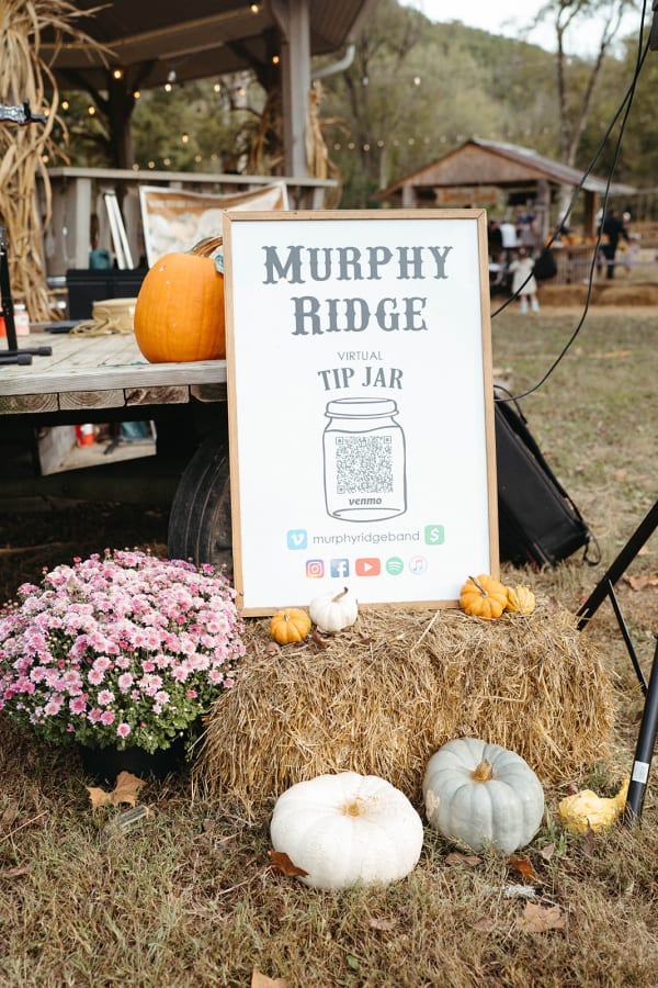 Band tip-jar sign with mums and white pumpkins on a hay bale