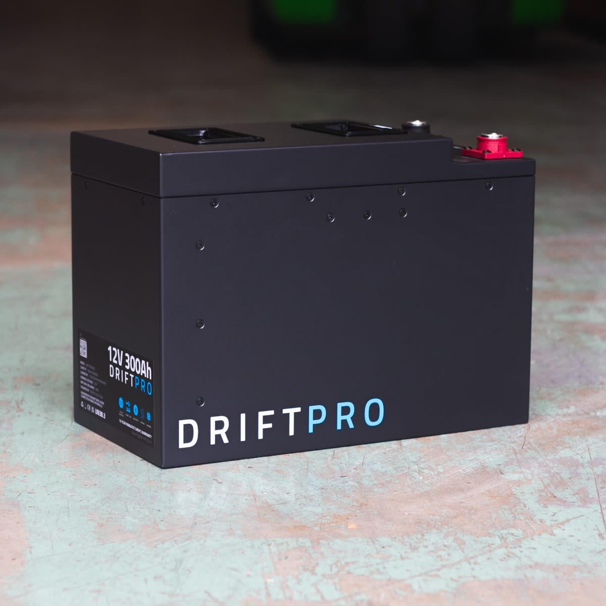 A black Fogstar Drift PRO 300Ah - 12V lithium leisure battery with specifications "12V 300Ah" rests on a concrete floor.