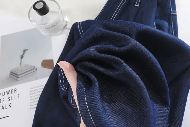 YEEYEEWang Wide-Leg Jeans in Denim Blue, Asian-fit cut, fabric gathered in one hand showing soft bunching and supple folds.