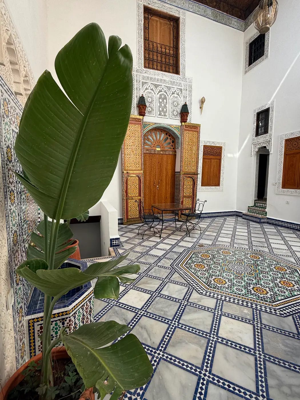 Le patio d'un riad : colonnes sculptées, lanterne en laiton et plantes vertes