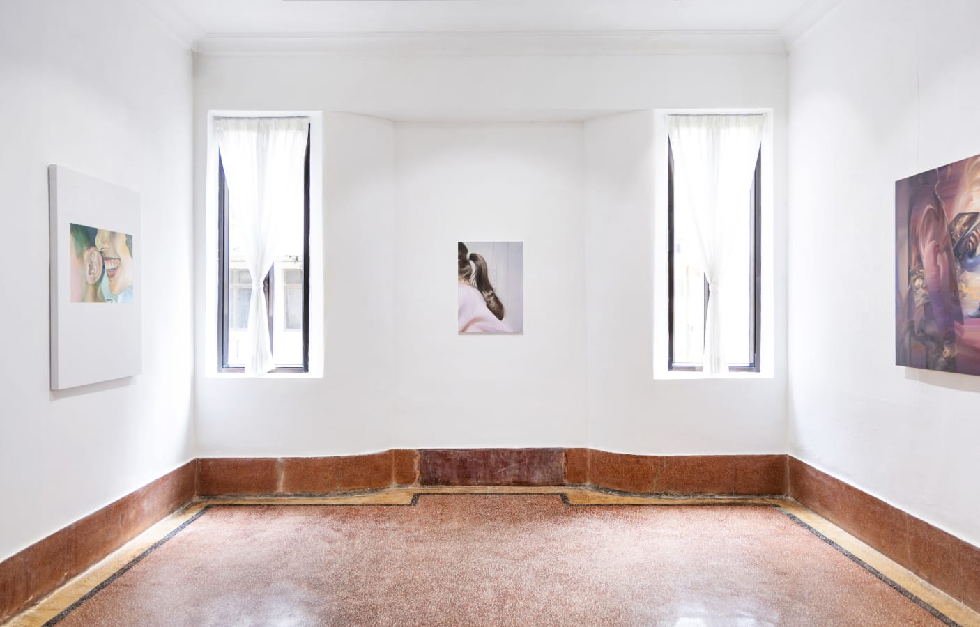 A white walled gallery with three artworks hung on the walls and two slim windows