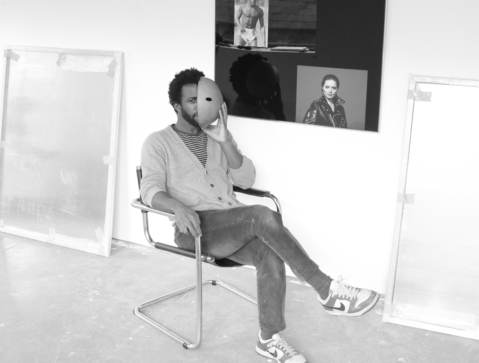 A portrait of Simeon Barclay sat in his studio holding a mask over his face
