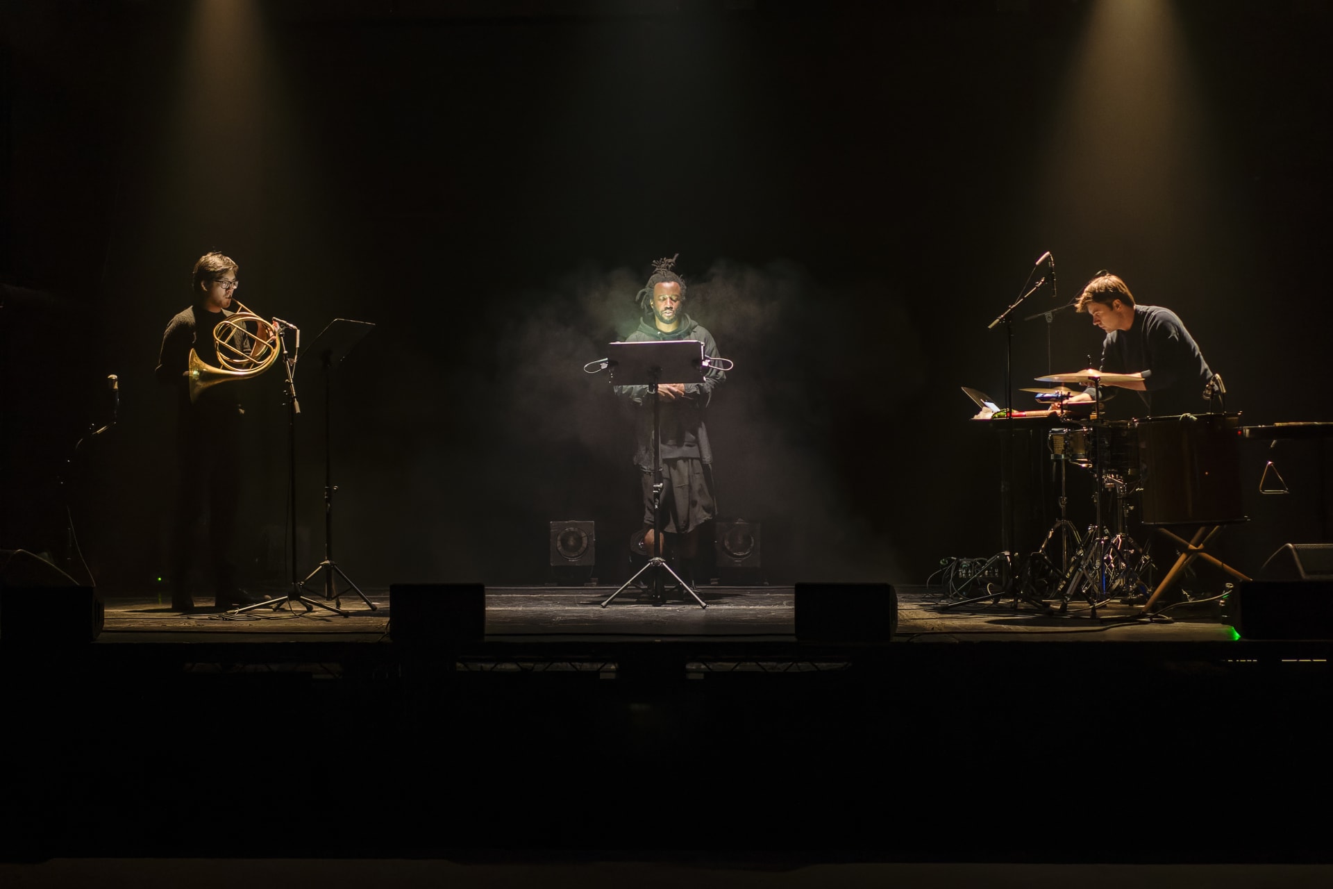 Simeon Barclay performing on a spotlit stage flanked by two musicians