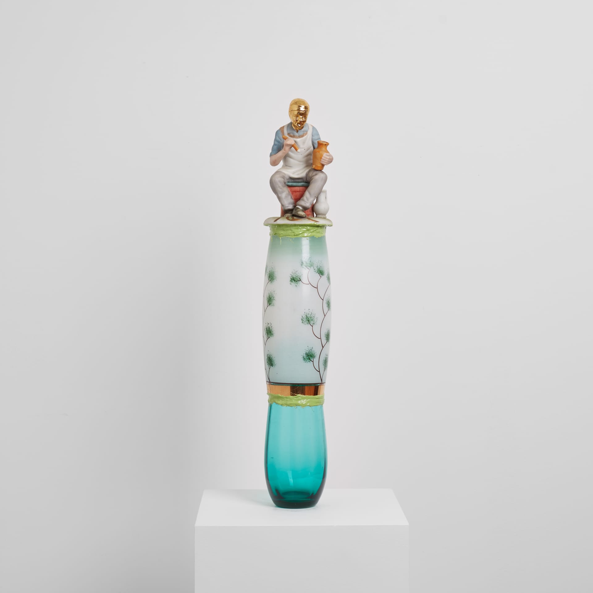 A sculpture by Eric Bainbridge made from ceramic and glass objects acquired by the artist that have been fused together by coloured resin. A figurine of an artisan with gold plated head sits on the top.