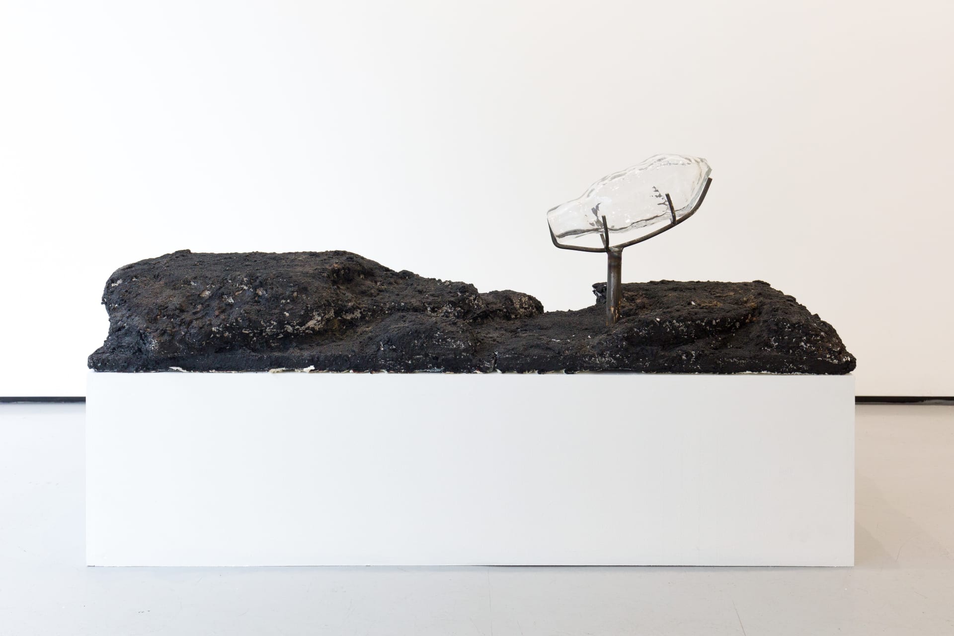 Blown glass vessels are held by metal structures above volcanic rock-like strata in this sculpture by Emii Alrai