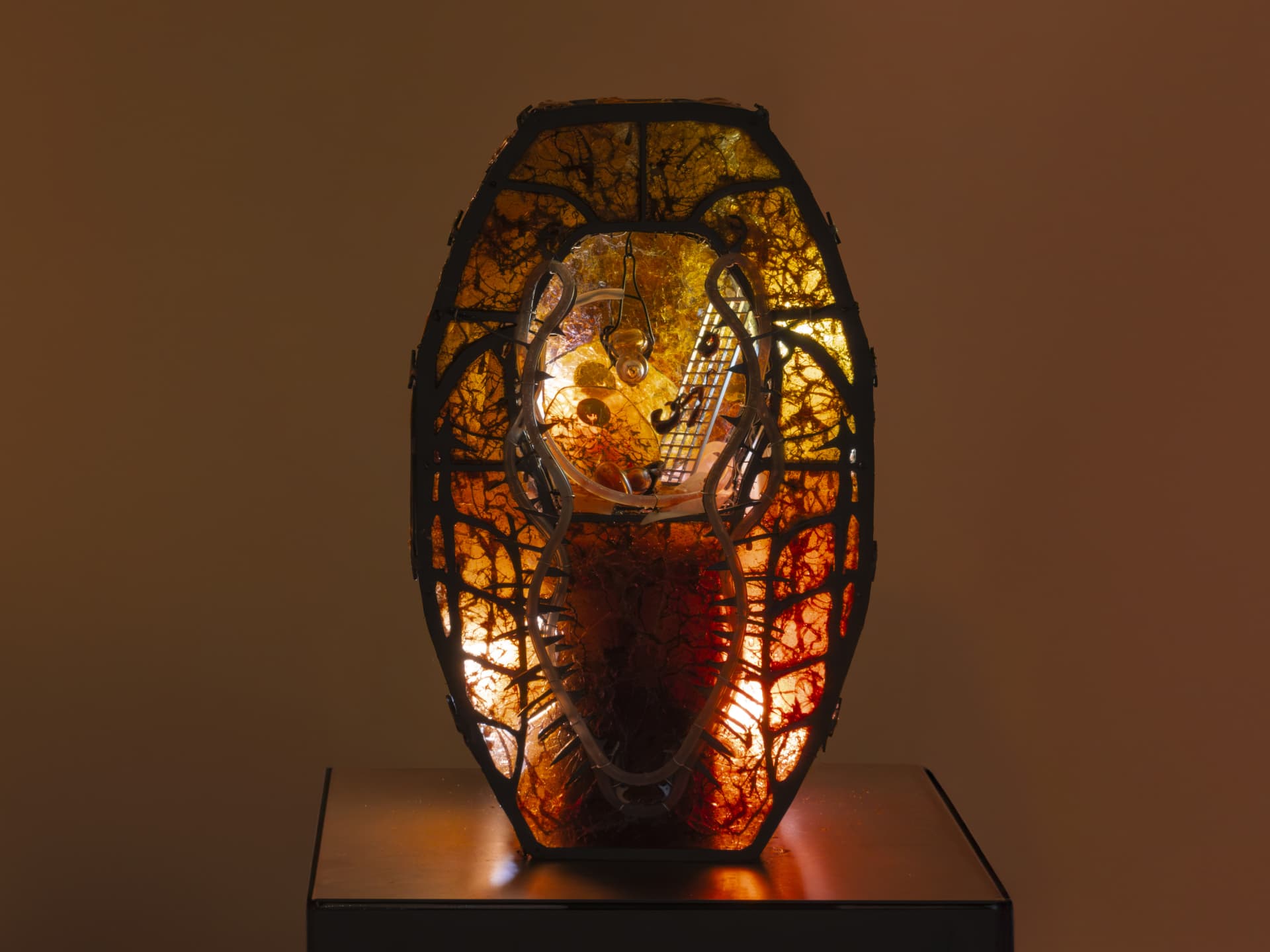 Sculpture by Hazel Brill. Made out of a metal frame and lit from the inside with amber light glowing through resin material. Has an open centre with steam rising from below. Gothic style.