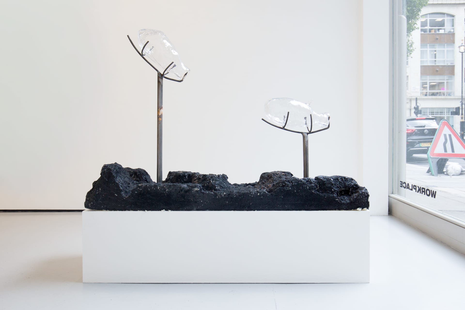 Blown glass vessels are held by metal structures above volcanic rock-like strata in this sculpture by Emii Alrai