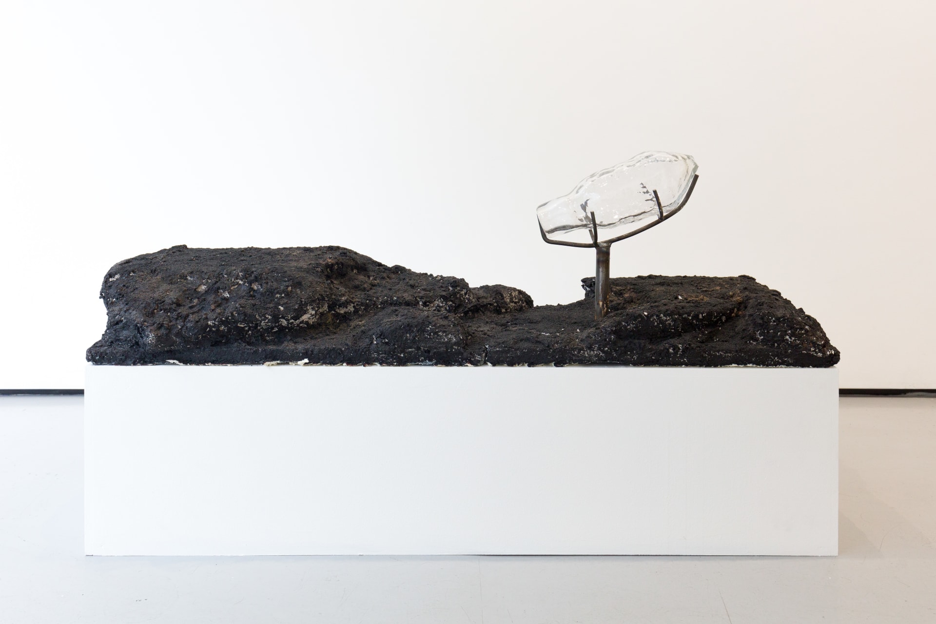 Blown glass vessels are held by metal structures above volcanic rock-like strata in this sculpture by Emii Alrai