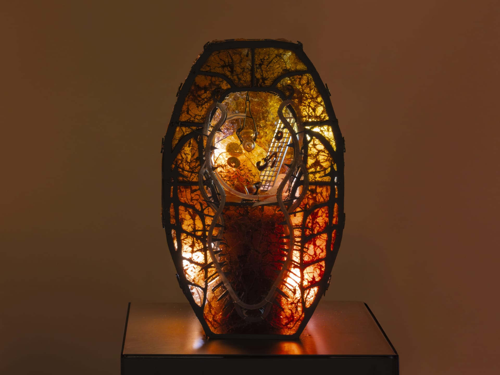 Sculpture by Hazel Brill. Made out of a metal frame and lit from the inside with amber light glowing through resin material. Has an open centre with steam rising from below. Gothic style.