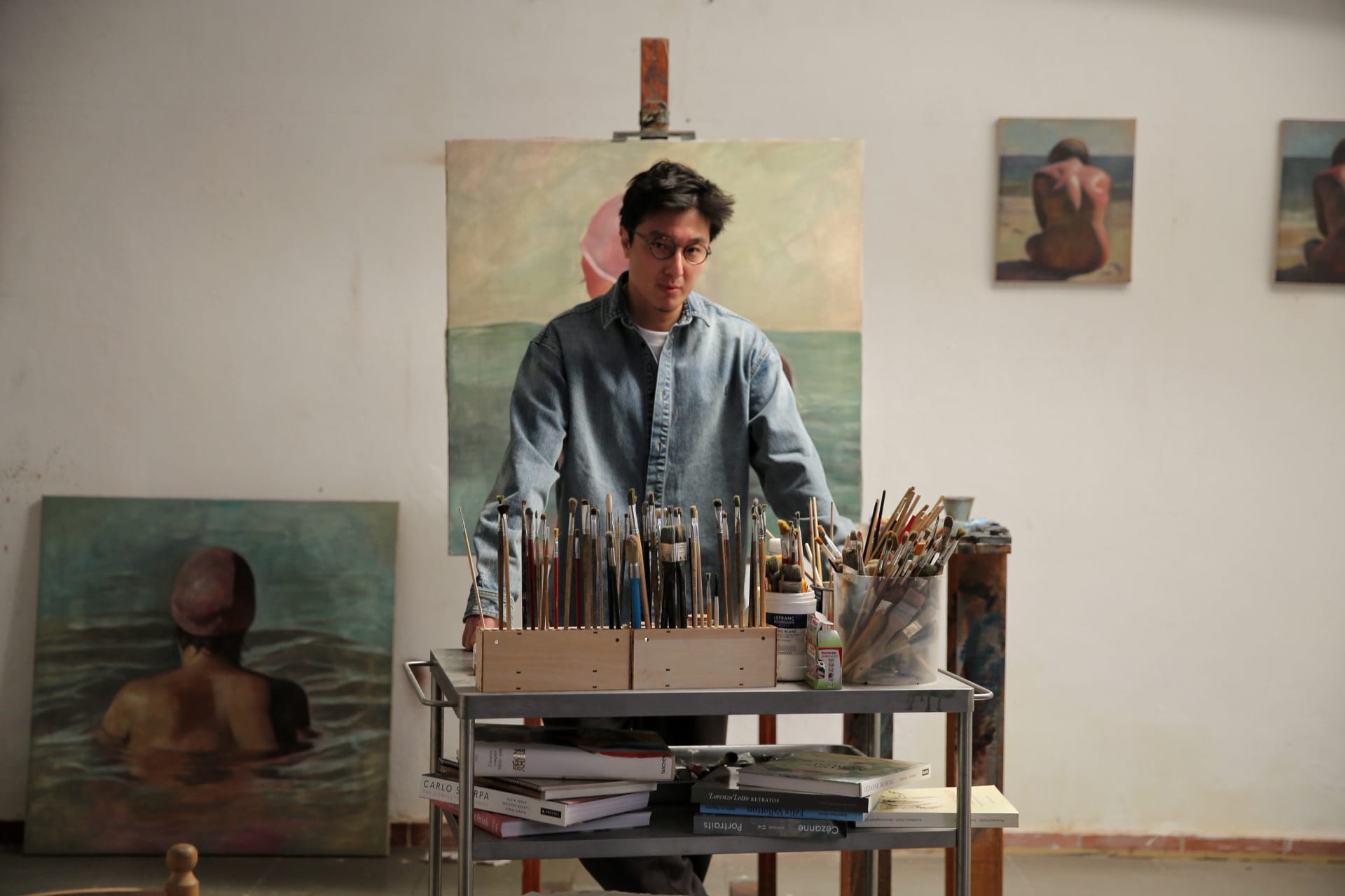Wang Pei stood in his studio infront of a metal trolley full of brushes and paints