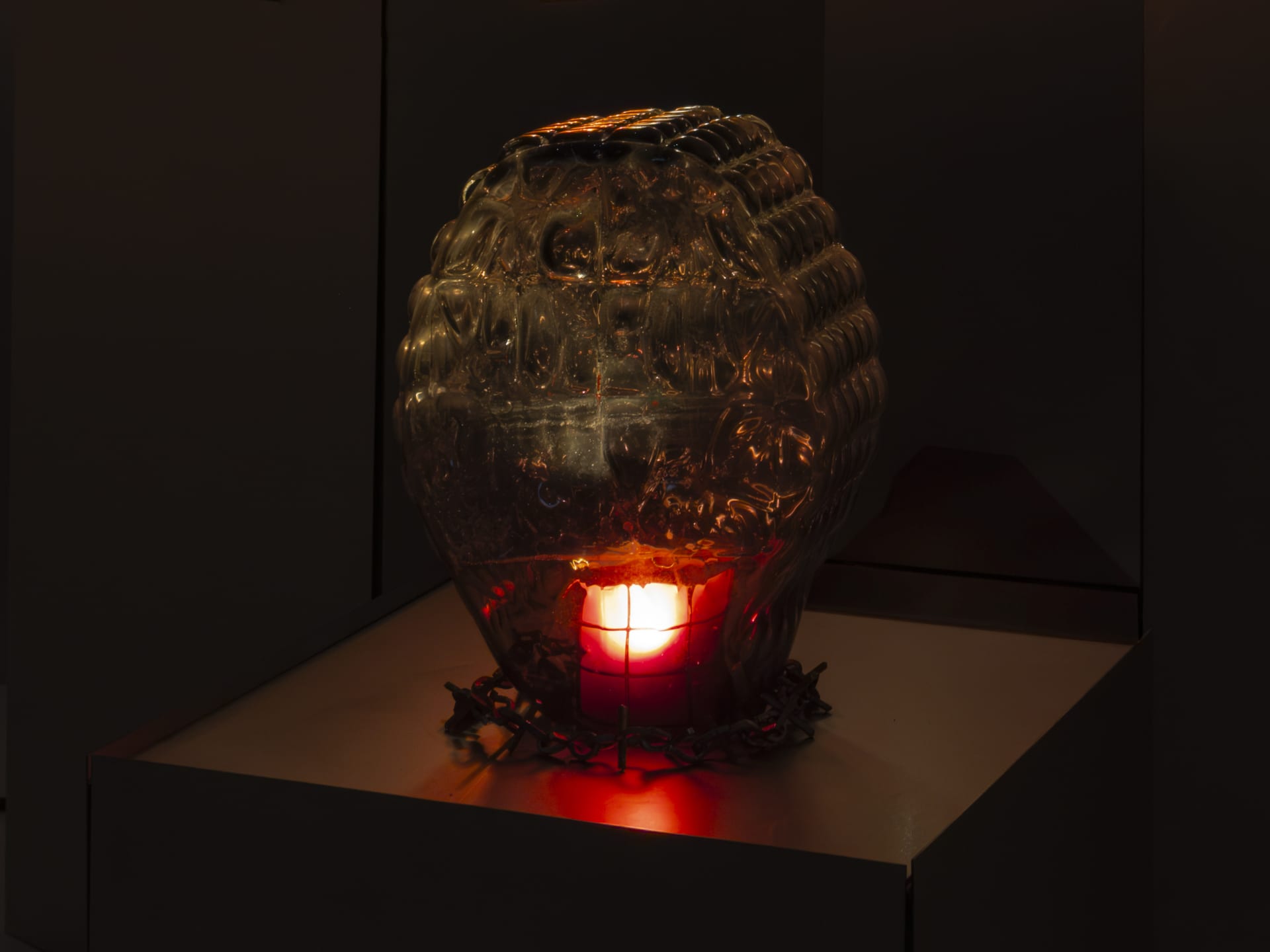 Sculpture by Hazel Brill made from a glass diamond shaped dome with raised circular bobble on the surface lit from the inside with a dim red light bulb.