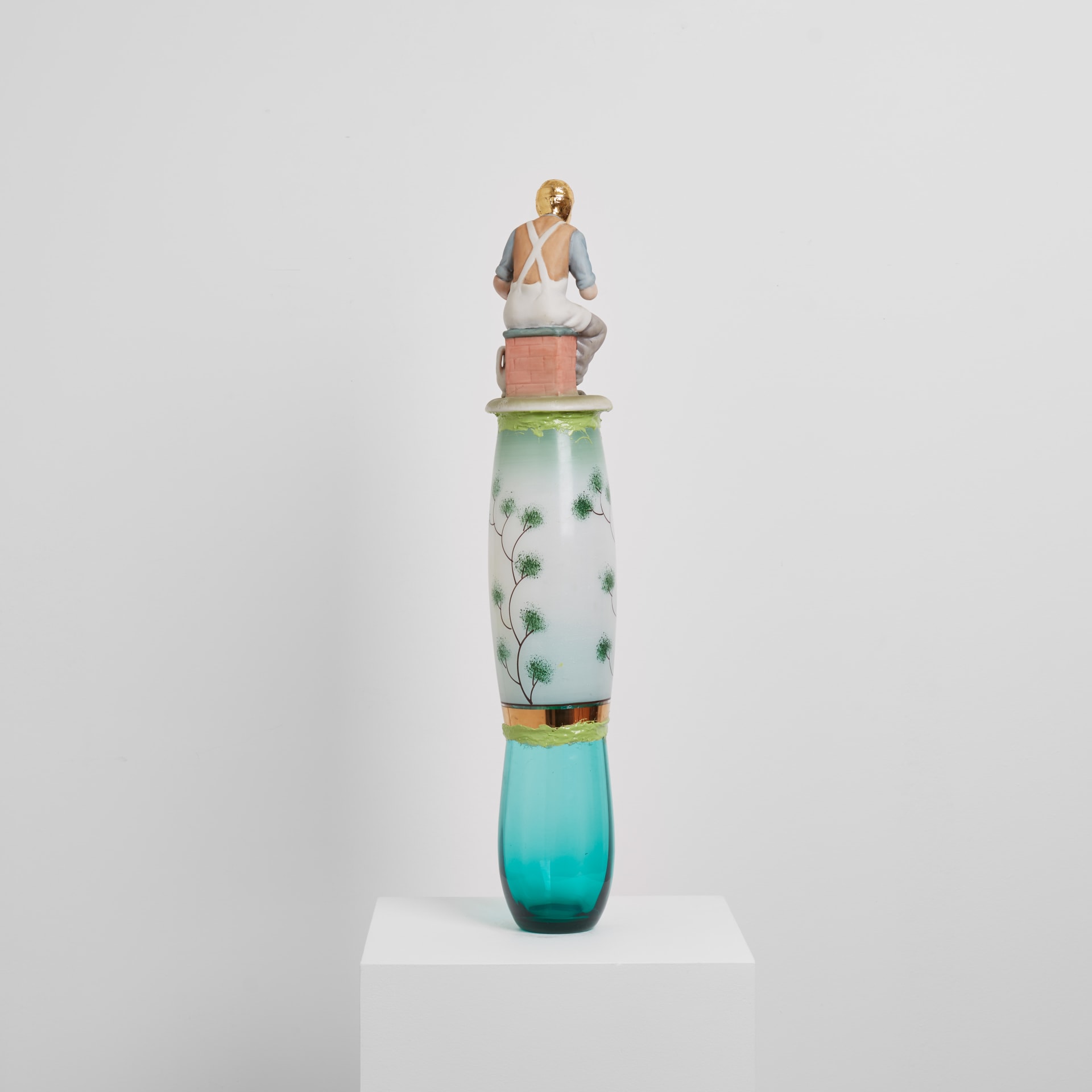 A sculpture by Eric Bainbridge made from ceramic and glass objects acquired by the artist that have been fused together by coloured resin. A figurine of an artisan with gold plated head sits on the top.