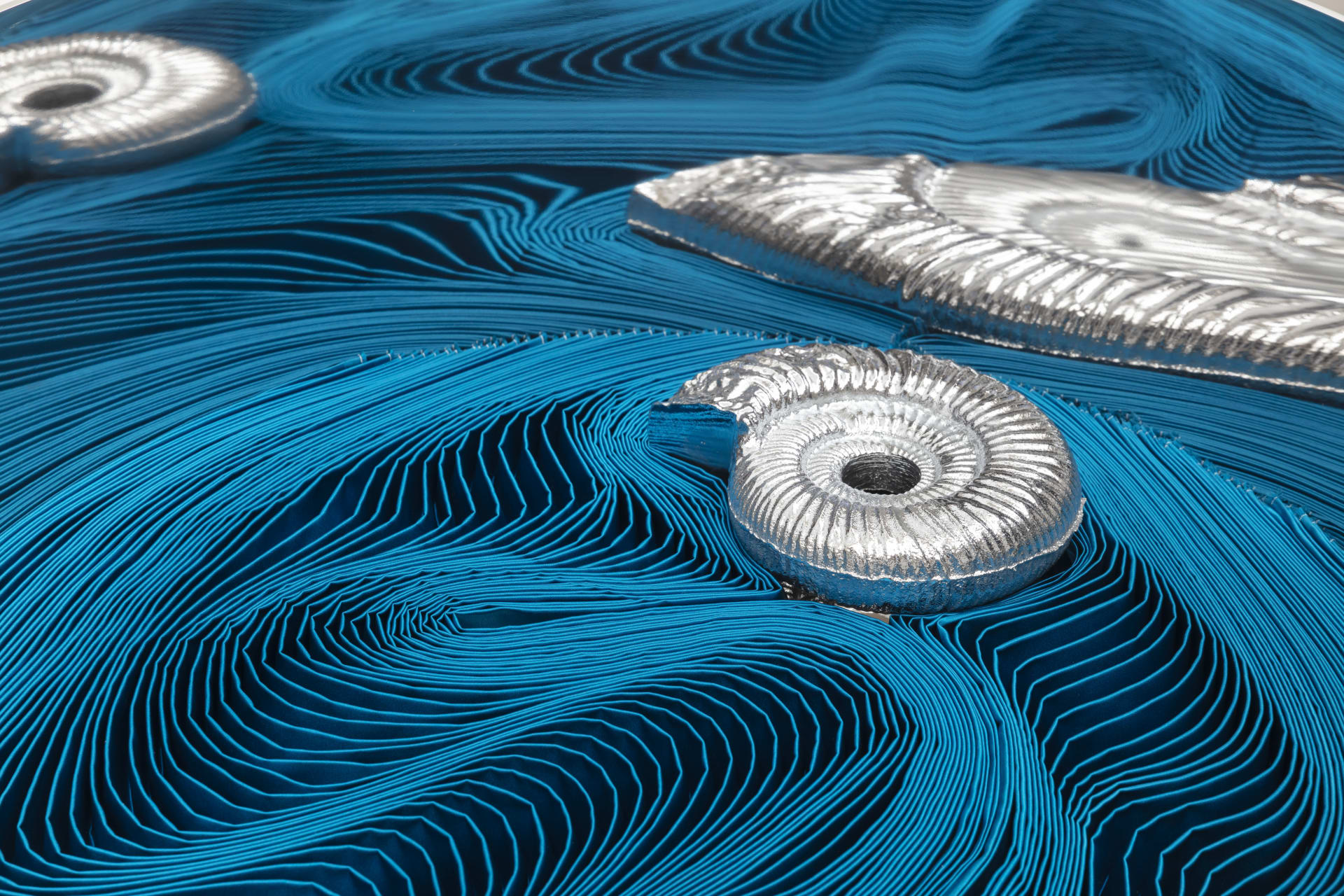 A detail of a sculpture by Alice Channer of pleated satin silk with cast silver ammonites sat on top