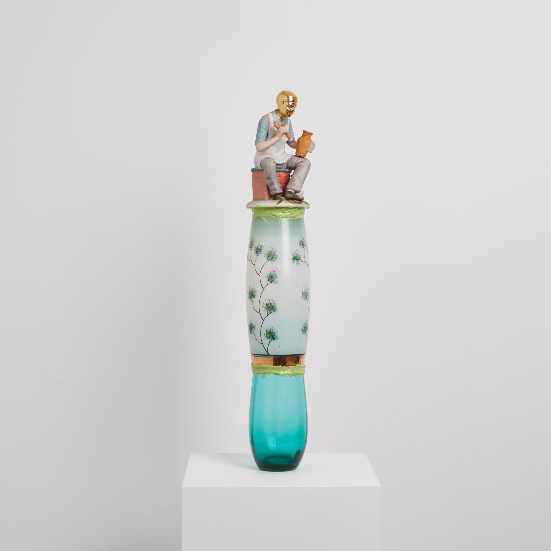 A sculpture by Eric Bainbridge made from ceramic and glass objects acquired by the artist that have been fused together by coloured resin. A figurine of an artisan with gold plated head sits on the top.