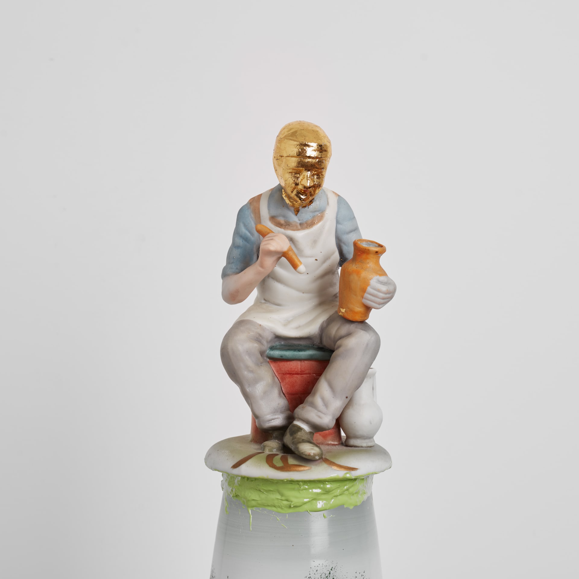 A sculpture by Eric Bainbridge made from ceramic and glass objects acquired by the artist that have been fused together by coloured resin. A figurine of an artisan with gold plated head sits on the top.